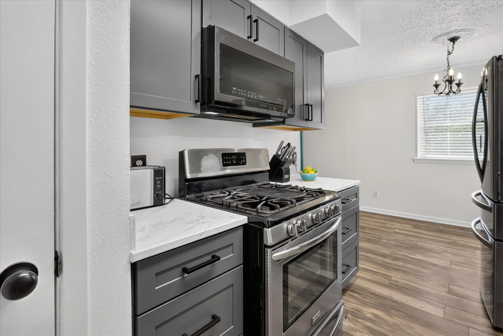 Stainless steel range with gas cooktop, sleek gray cabinetry, white countertops, built-in microwave, and wood-finish flooring
