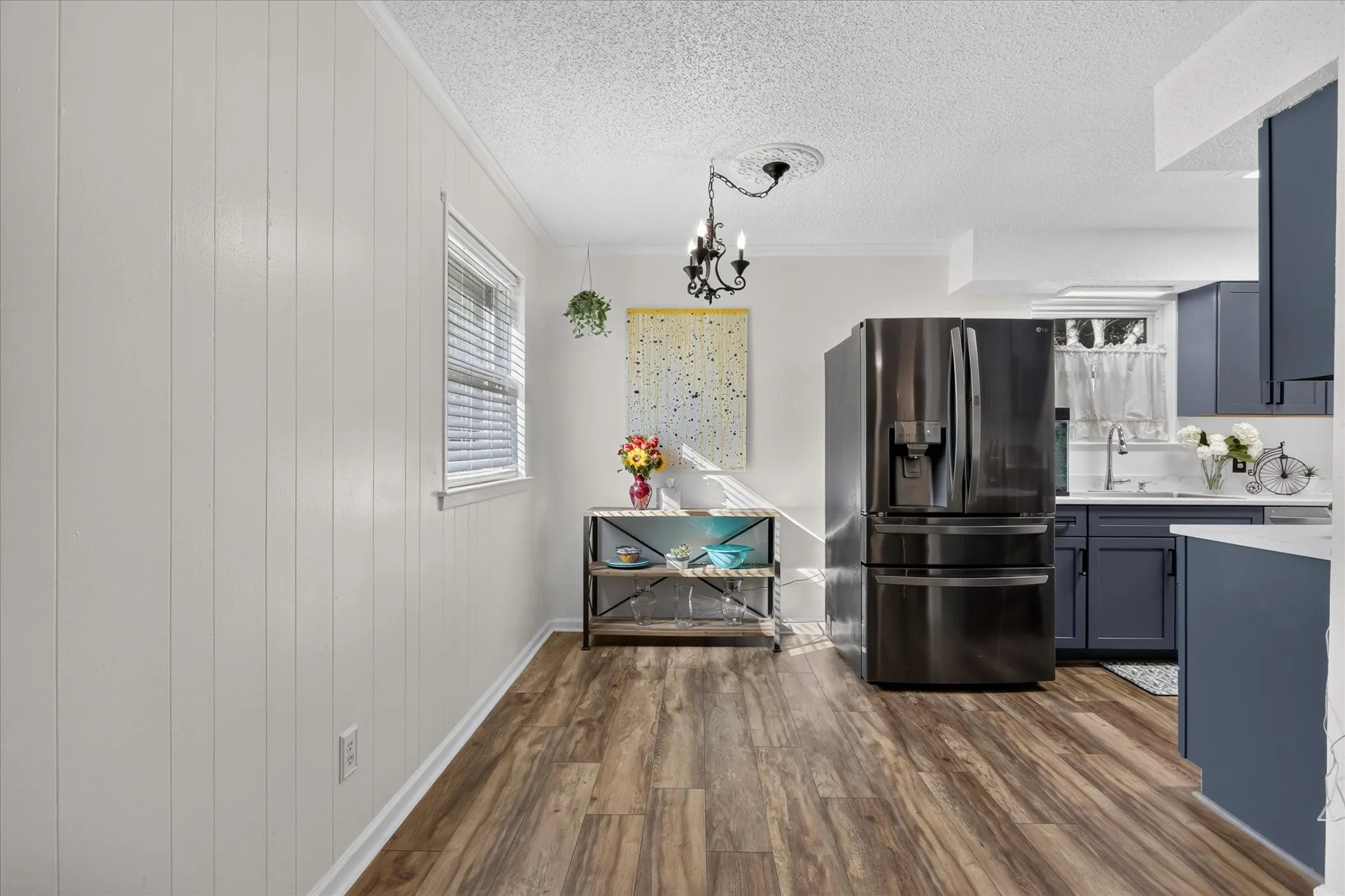 Wood-finish flooring, white paneled wall, black appliance package, blue cabinetry, and white countertops