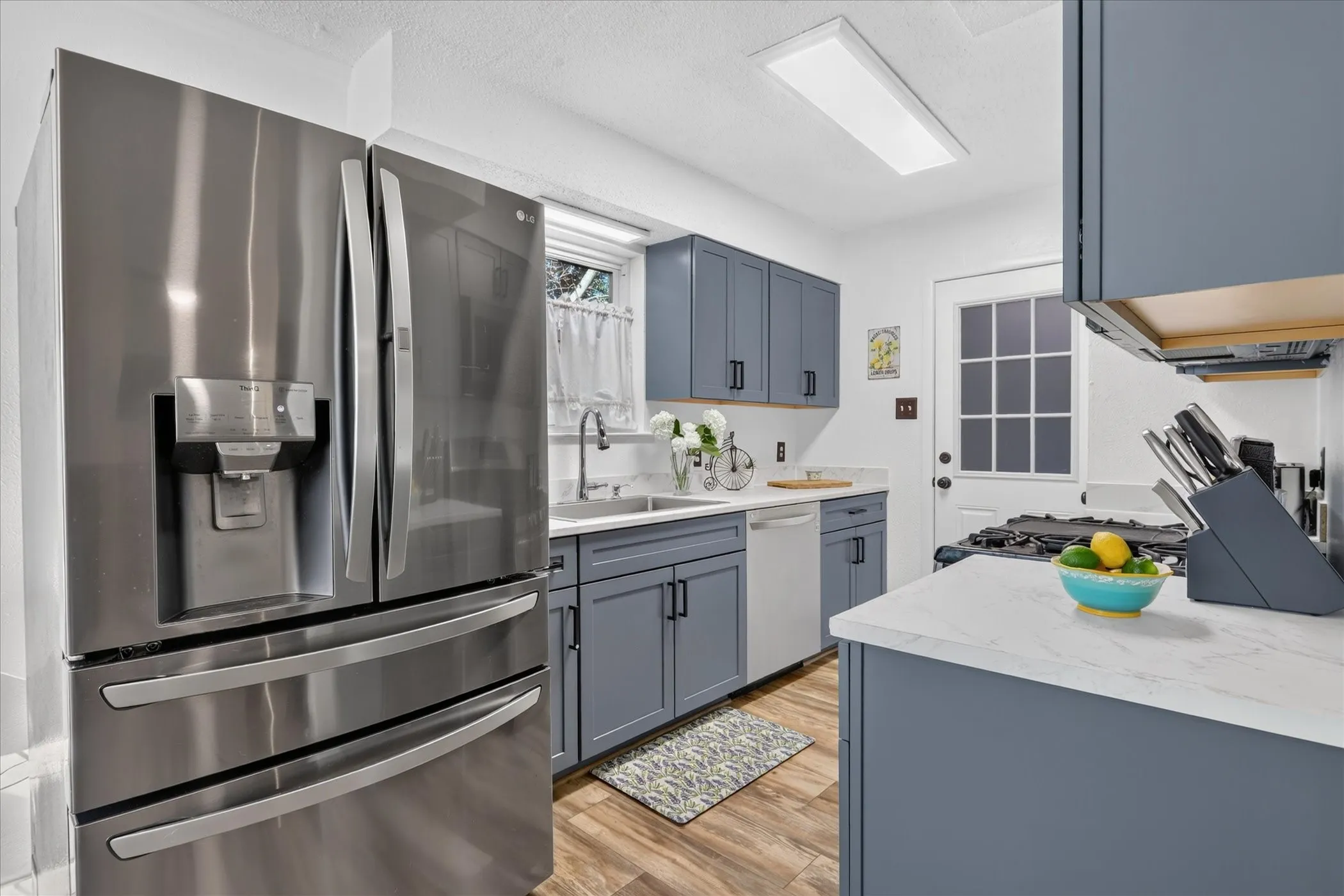 Stainless steel French door refrigerator, white countertops, gray cabinetry with black hardware, wood-finish flooring, and a white paneled door