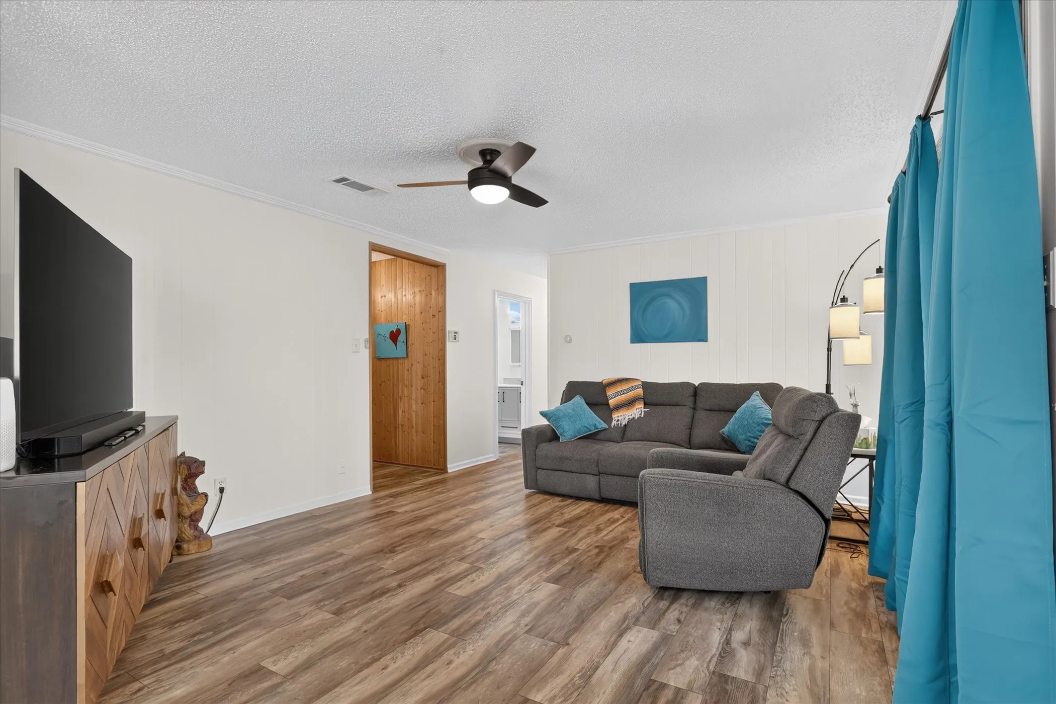 Wood-finish flooring throughout, white painted walls, and a ceiling fan with integrated lighting