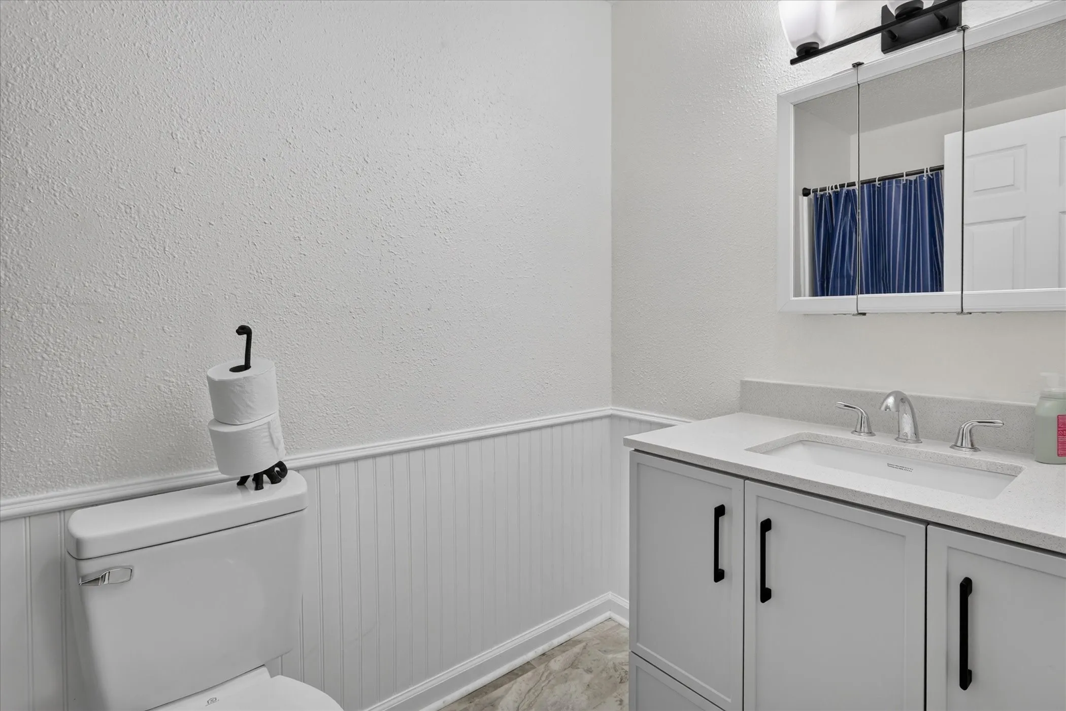 White shaker-style vanity with dark hardware, integrated sink, and a light-toned countertop
