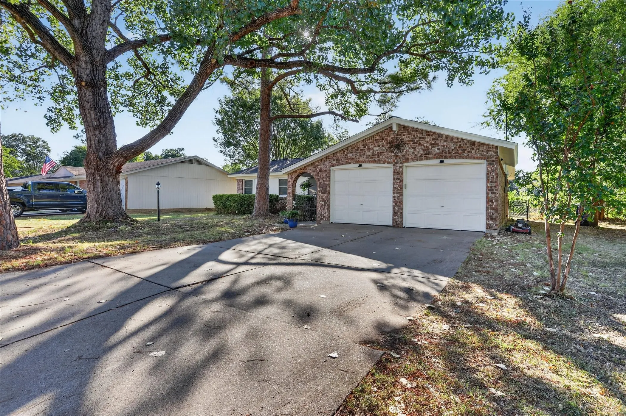 Brick facade with a two-car garage, concrete driveway, and mature trees