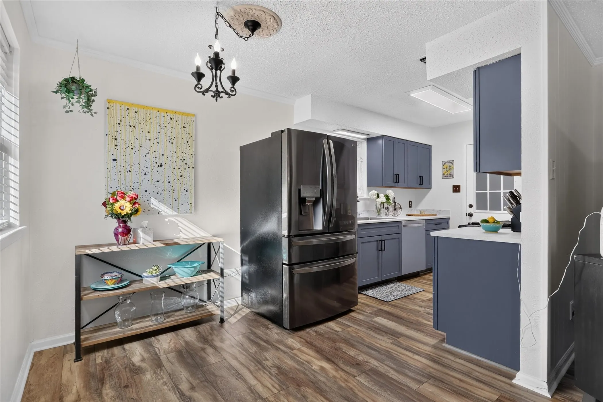 Wood-finish flooring, dark-toned refrigerator, gray cabinetry, white countertops, and a black chandelier