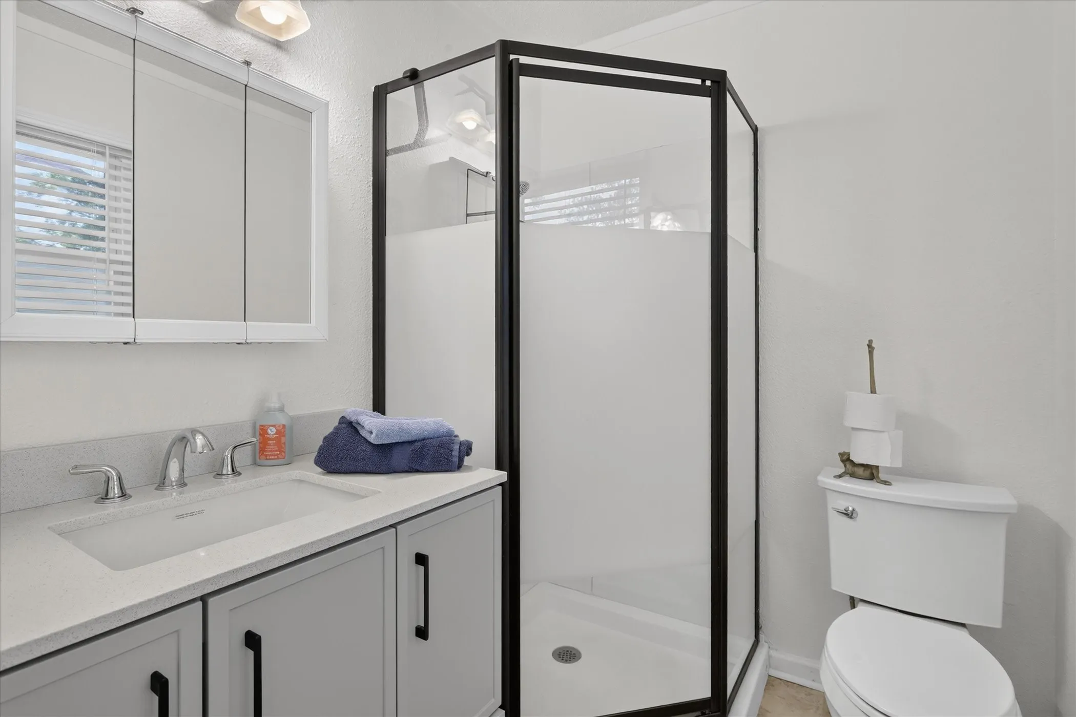 Single vanity with an integrated sink, polished chrome faucet, and light gray cabinetry with black pull hardware