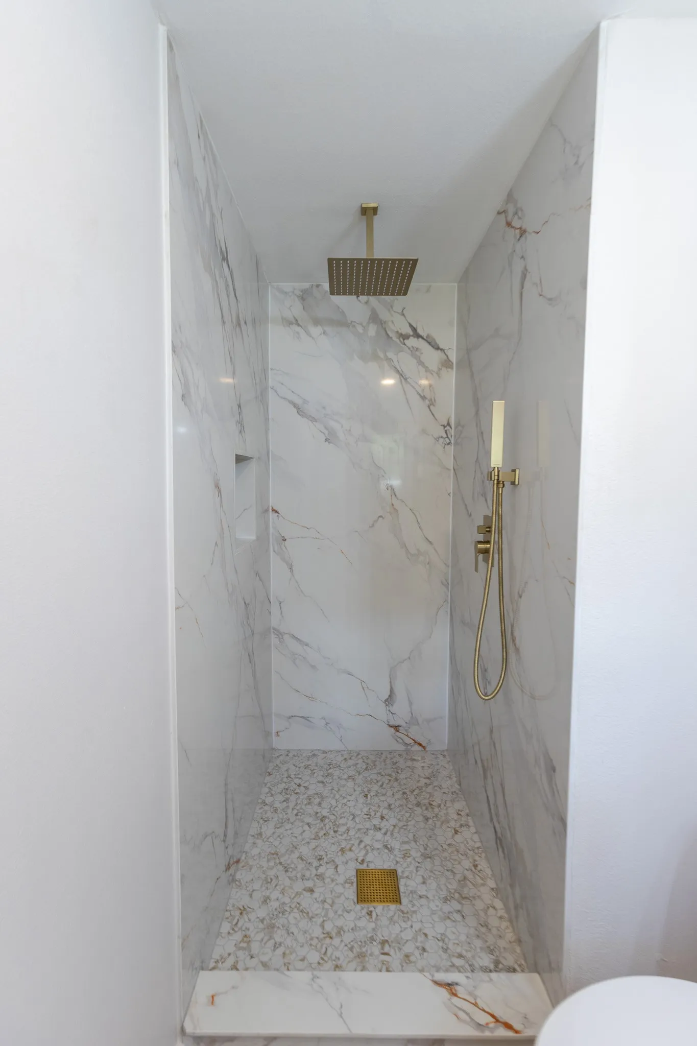 Walk-in shower with marble-look wall tiling, mosaic tile flooring, a recessed niche, and a gold-finish rainfall showerhead