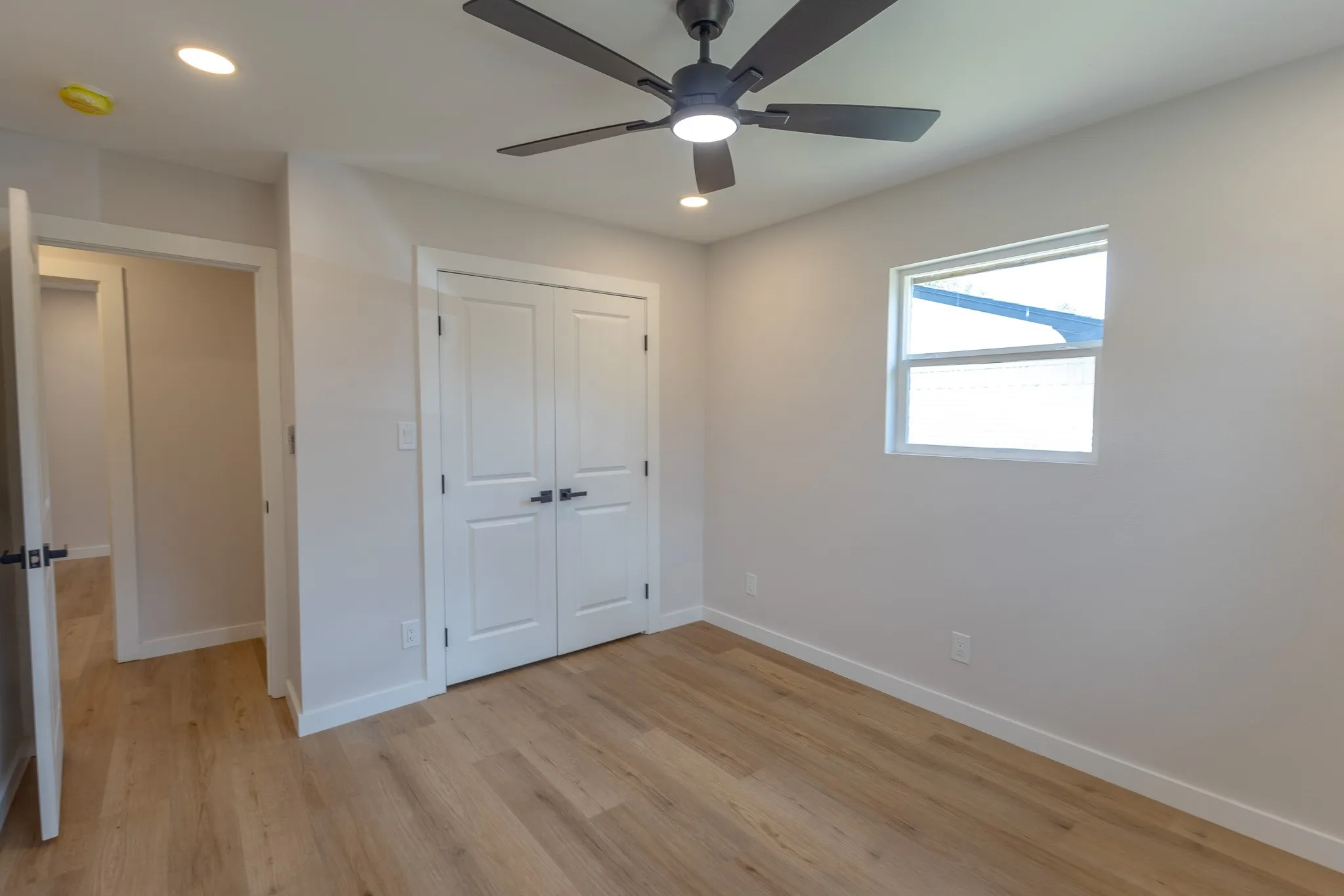Recessed ceiling lighting, wood-finish flooring, white double-panel doors, single window, and a ceiling fan with integrated lighting