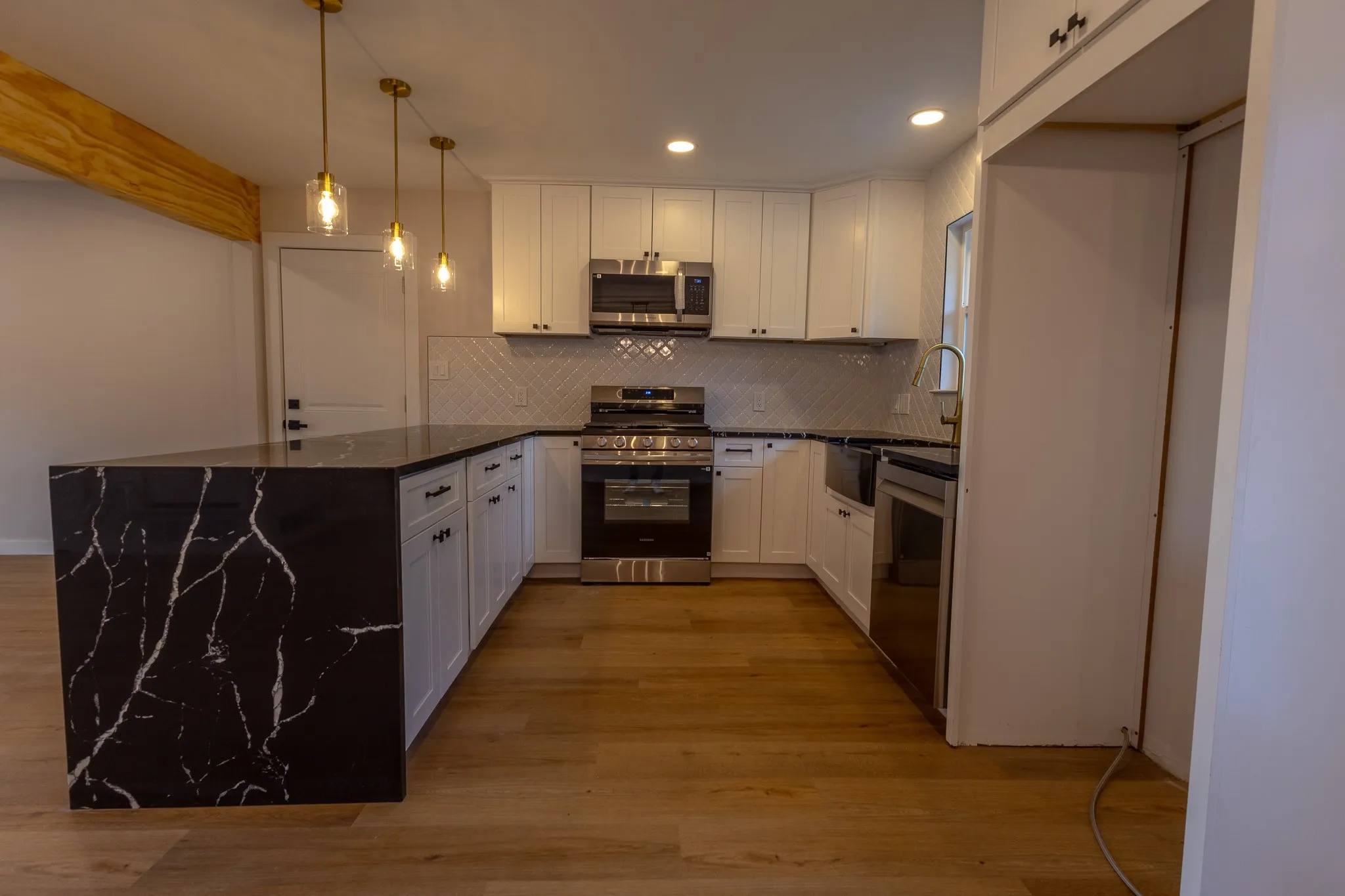 Kitchen featuring white cabinetry, dark countertops, stainless steel appliances, a tile backsplash, and wood-finish flooring