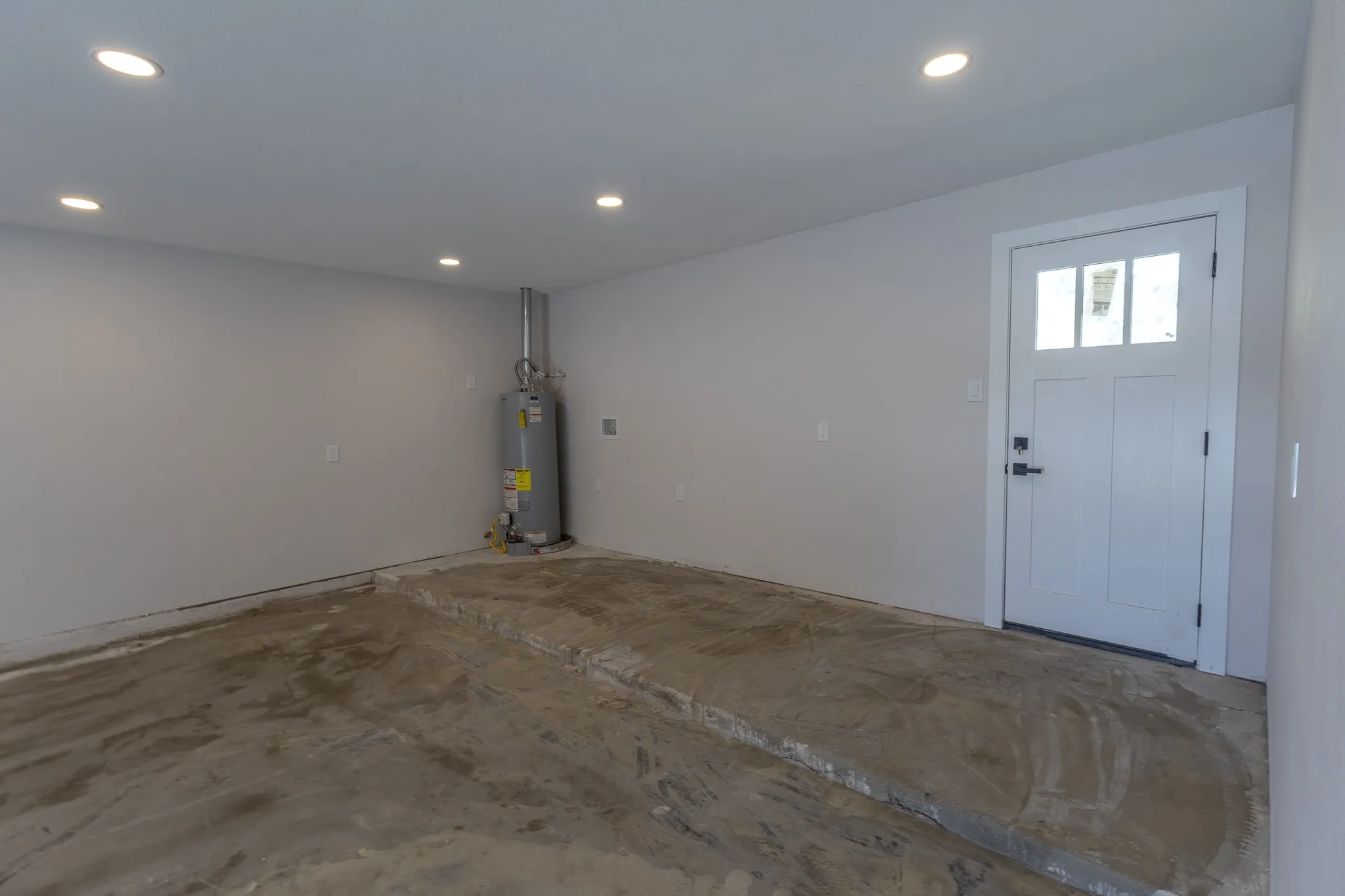 Recessed ceiling lighting, white paneled door with lites, concrete flooring, water heater, and light gray wall paint