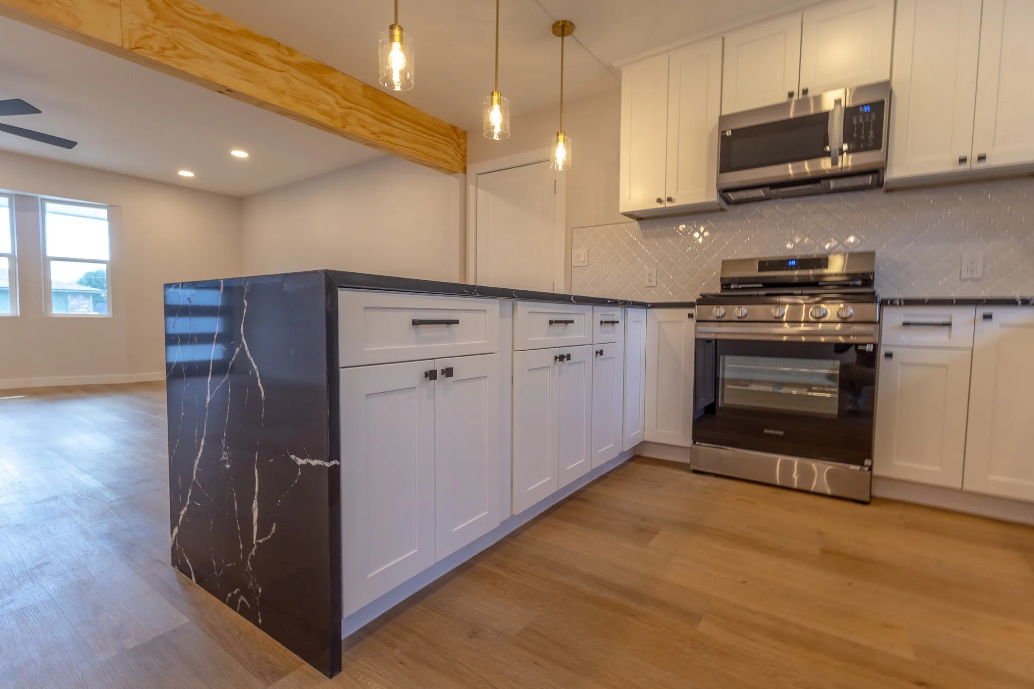 Kitchen featuring white shaker cabinetry, stainless steel appliances, dark countertops, and wood-finish flooring