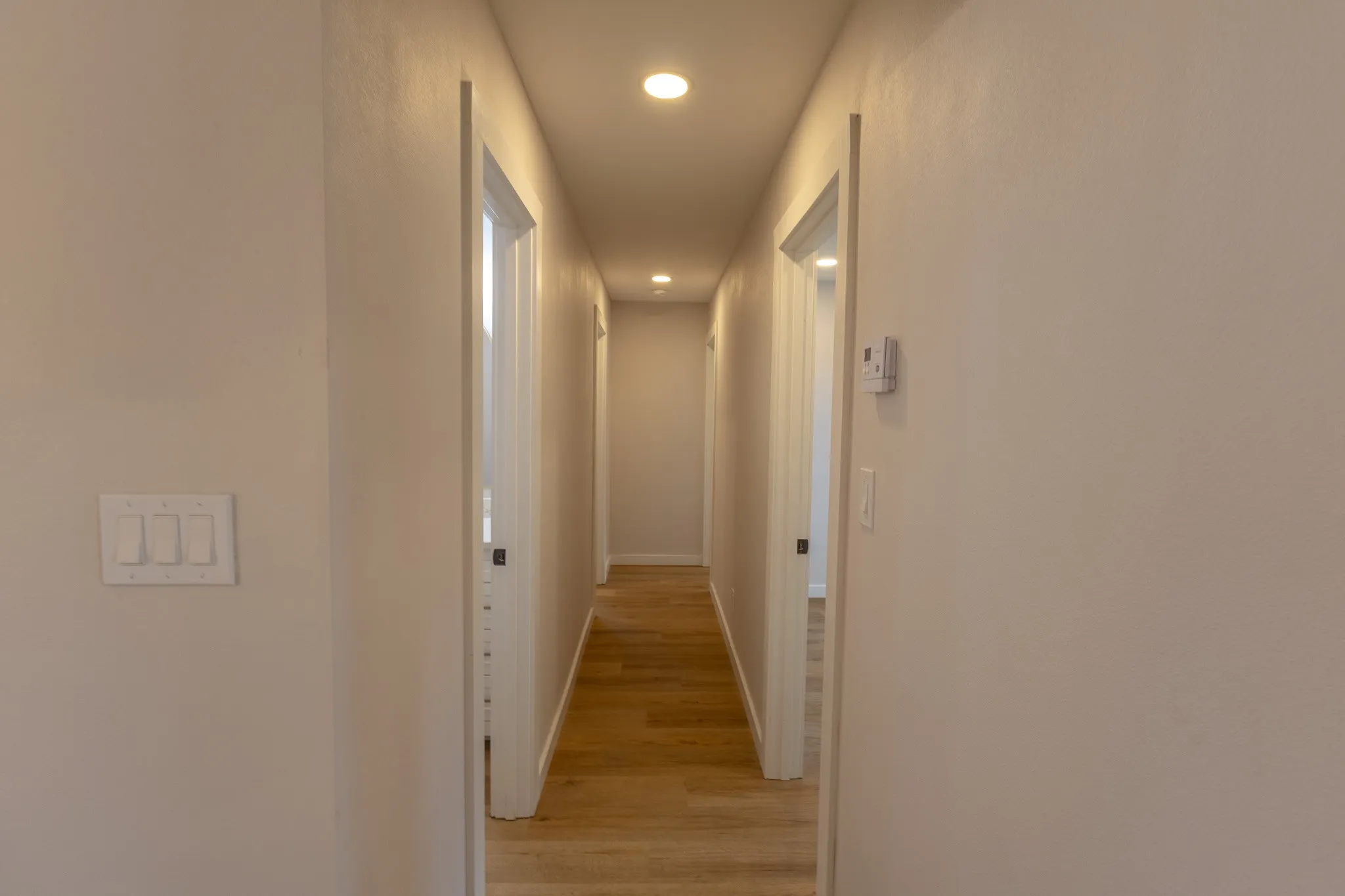 Recessed lighting illuminates the hallway, featuring wood-finish flooring and light-toned wall paint