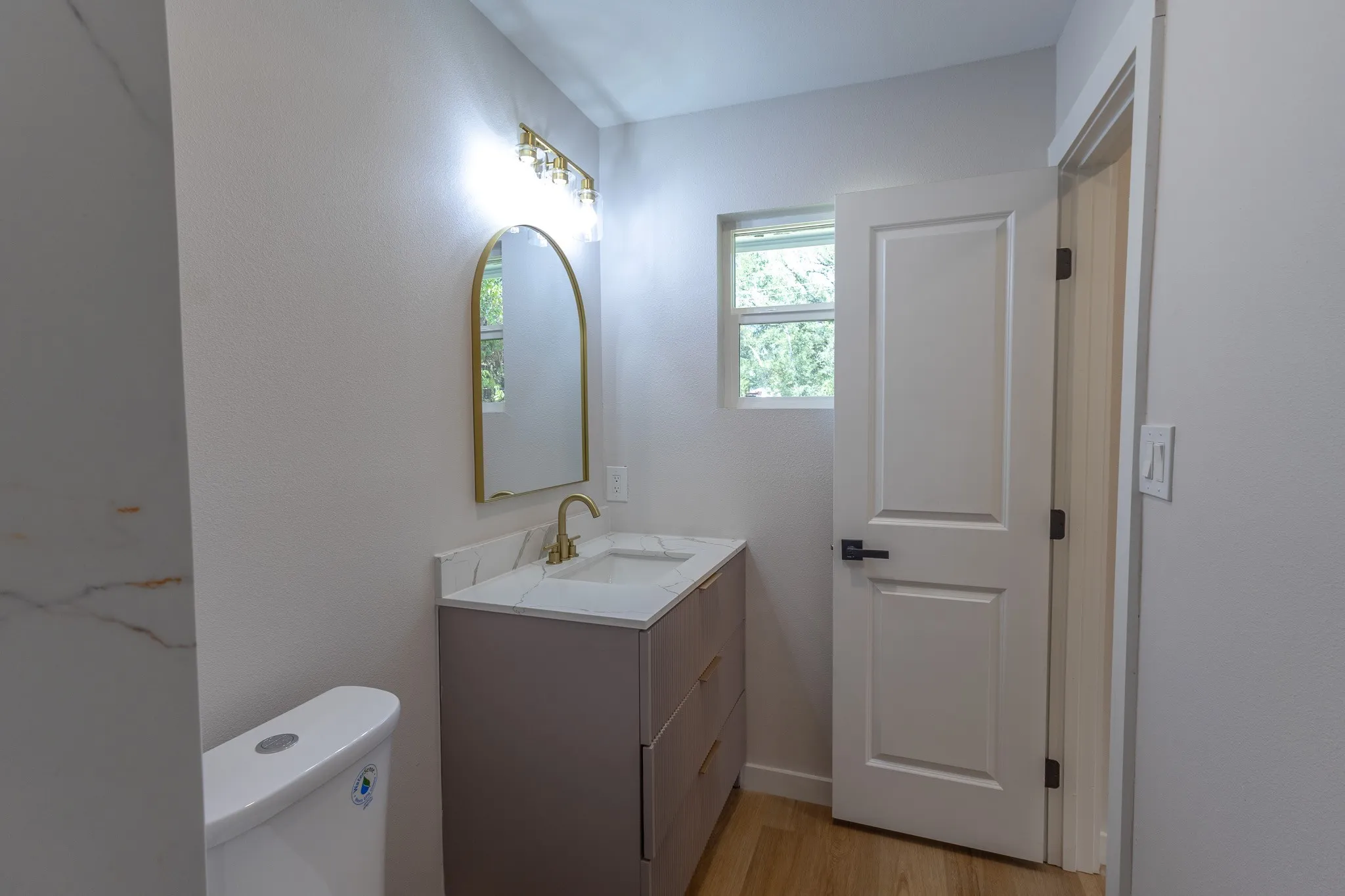 Modern vanity with an integrated sink, polished gold-tone faucet, arched mirror, and multi-bulb light fixture