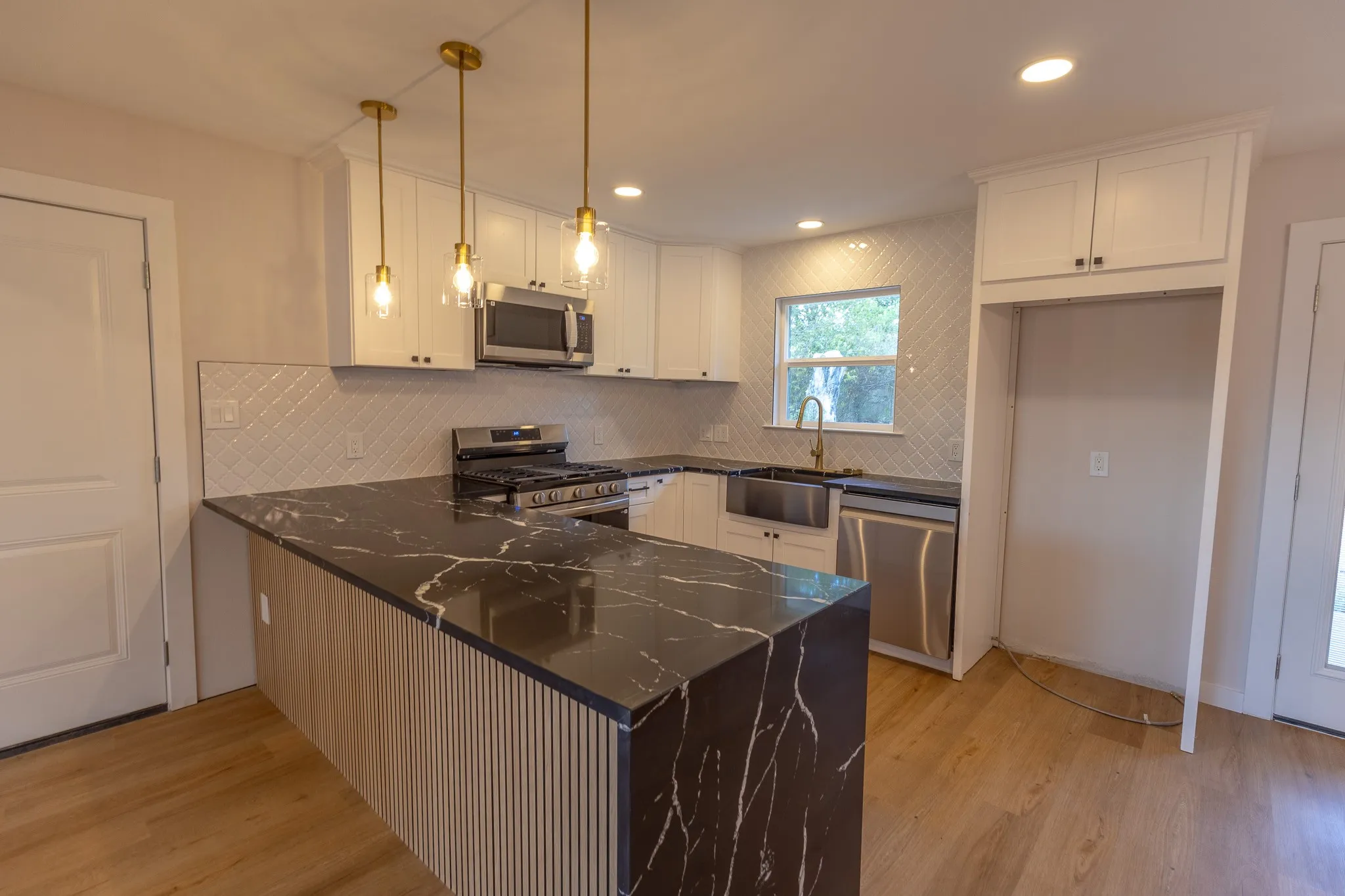 Kitchen featuring a U-shaped countertop with a waterfall edge, white shaker cabinetry, stainless steel appliances, and wood-finish flooring