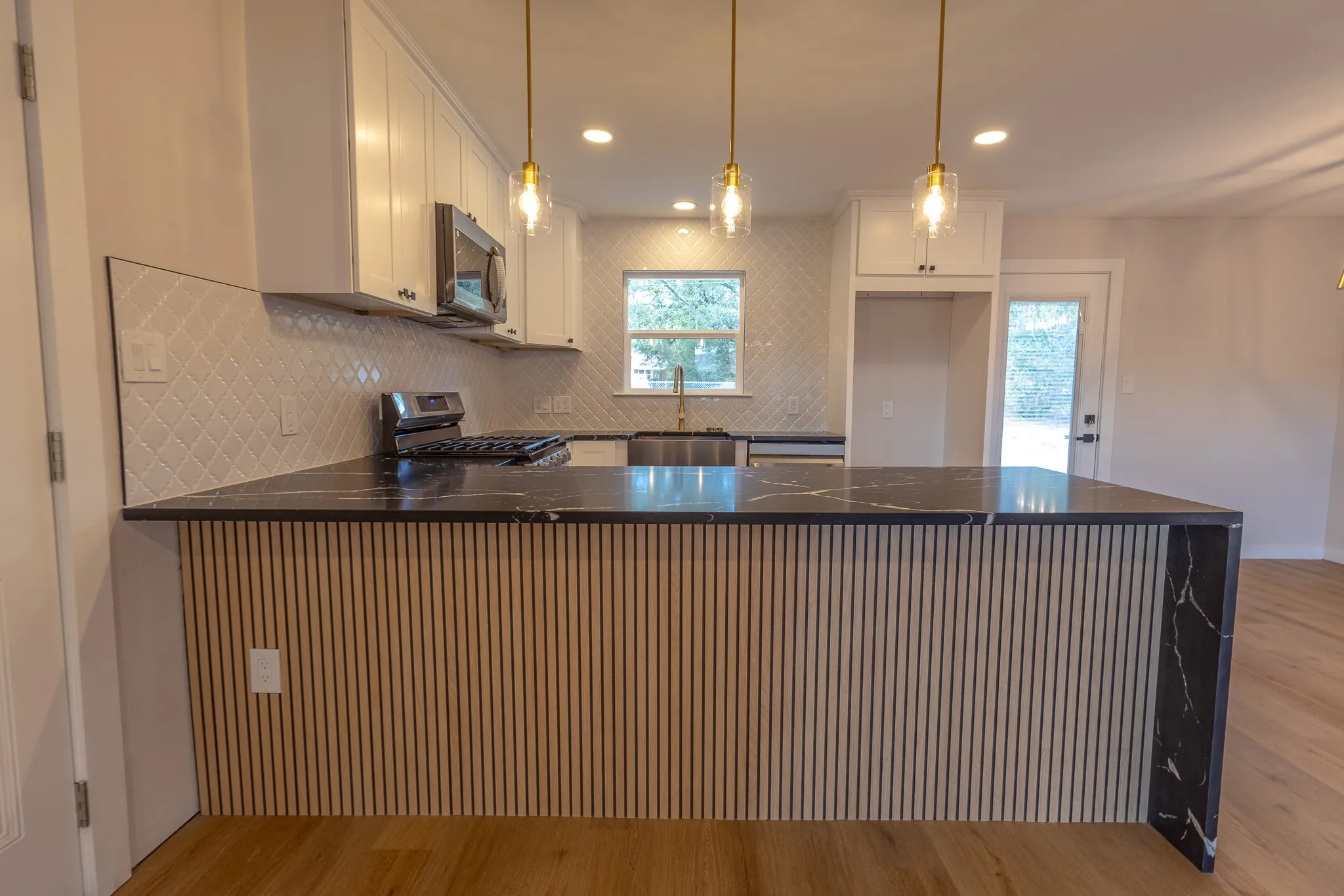 Kitchen featuring a waterfall island with wood slat detail, dark stone countertops, white shaker cabinetry, and a geometric tile backsplash