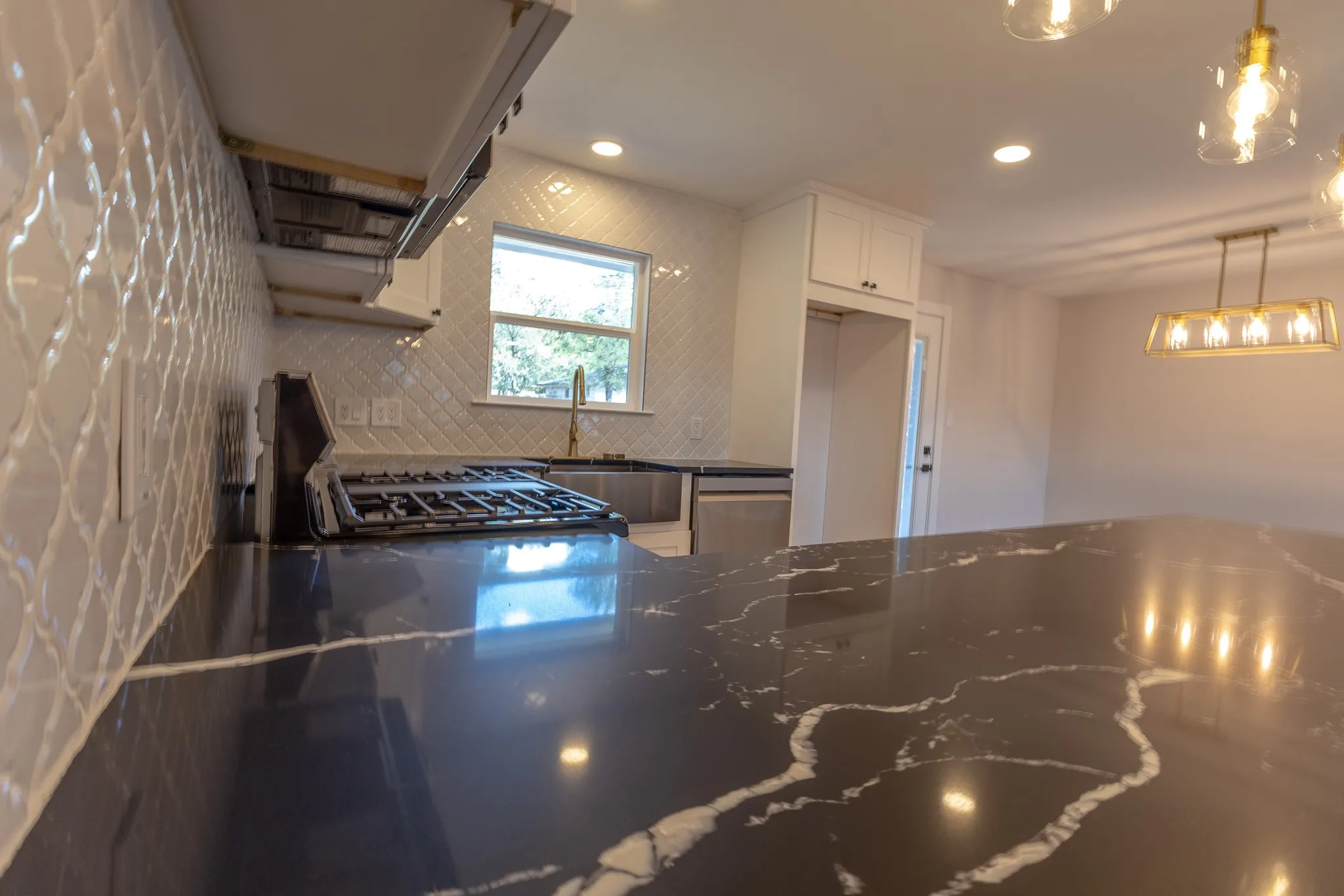 Kitchen featuring dark countertops with white veining, gas range with stainless steel hood, white arabesque tile backsplash, and recessed lighting