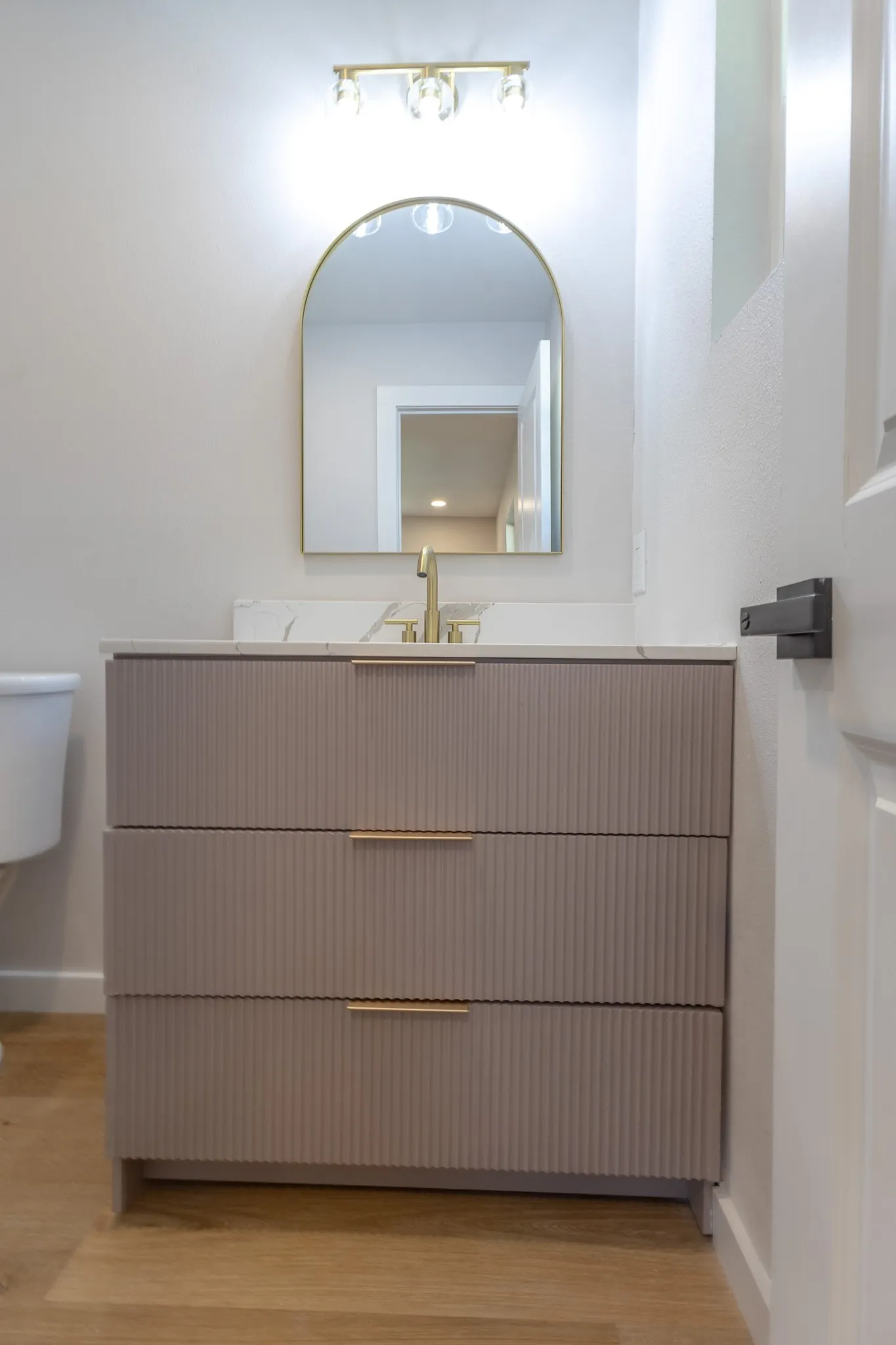 Vanity with textured drawer fronts, gold-tone hardware, and a white countertop