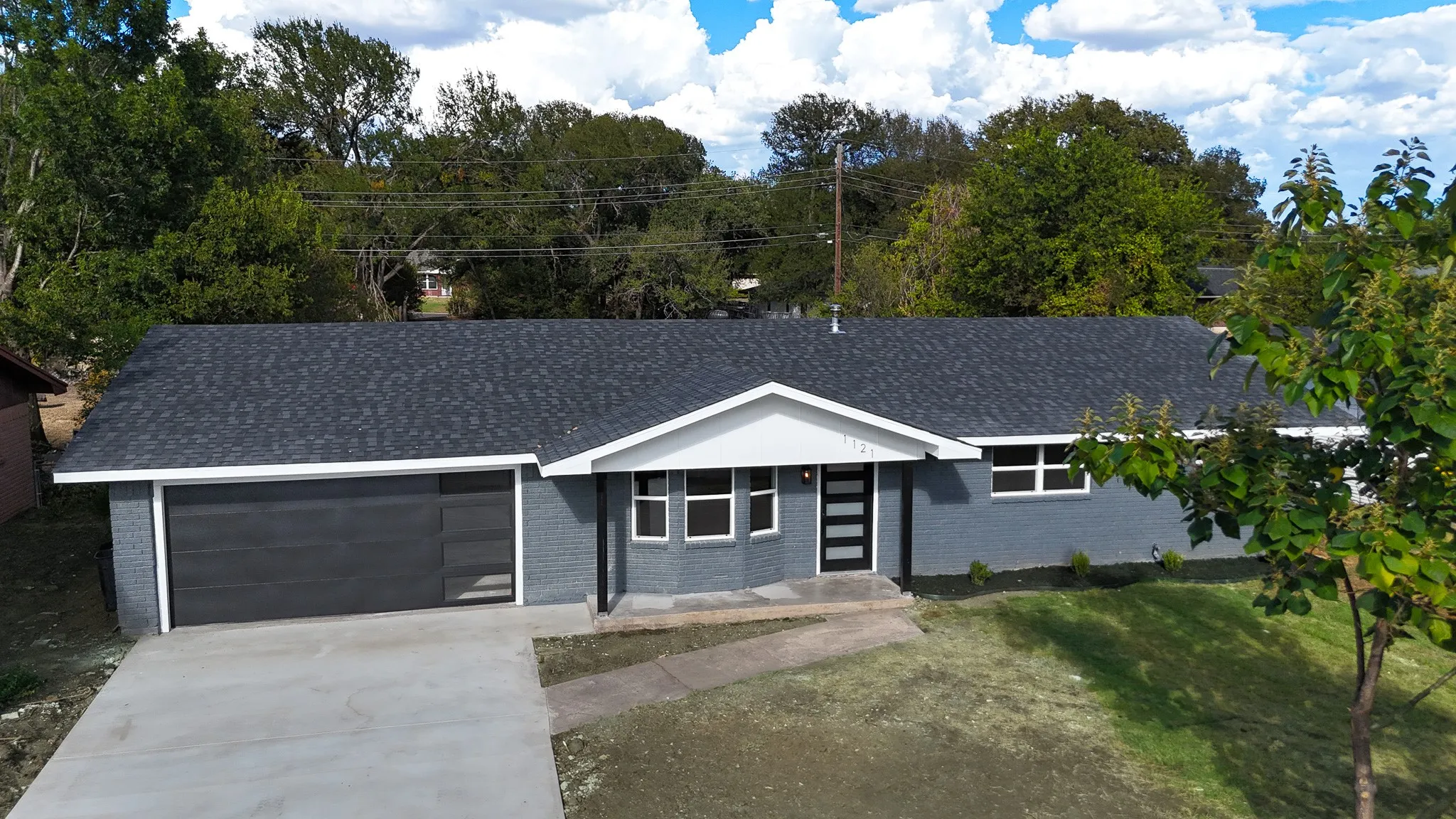 Single-story residence featuring a dark gray brick exterior, a newly installed dark shingle roof, and an attached two-car garage with a contemporary dark panel door