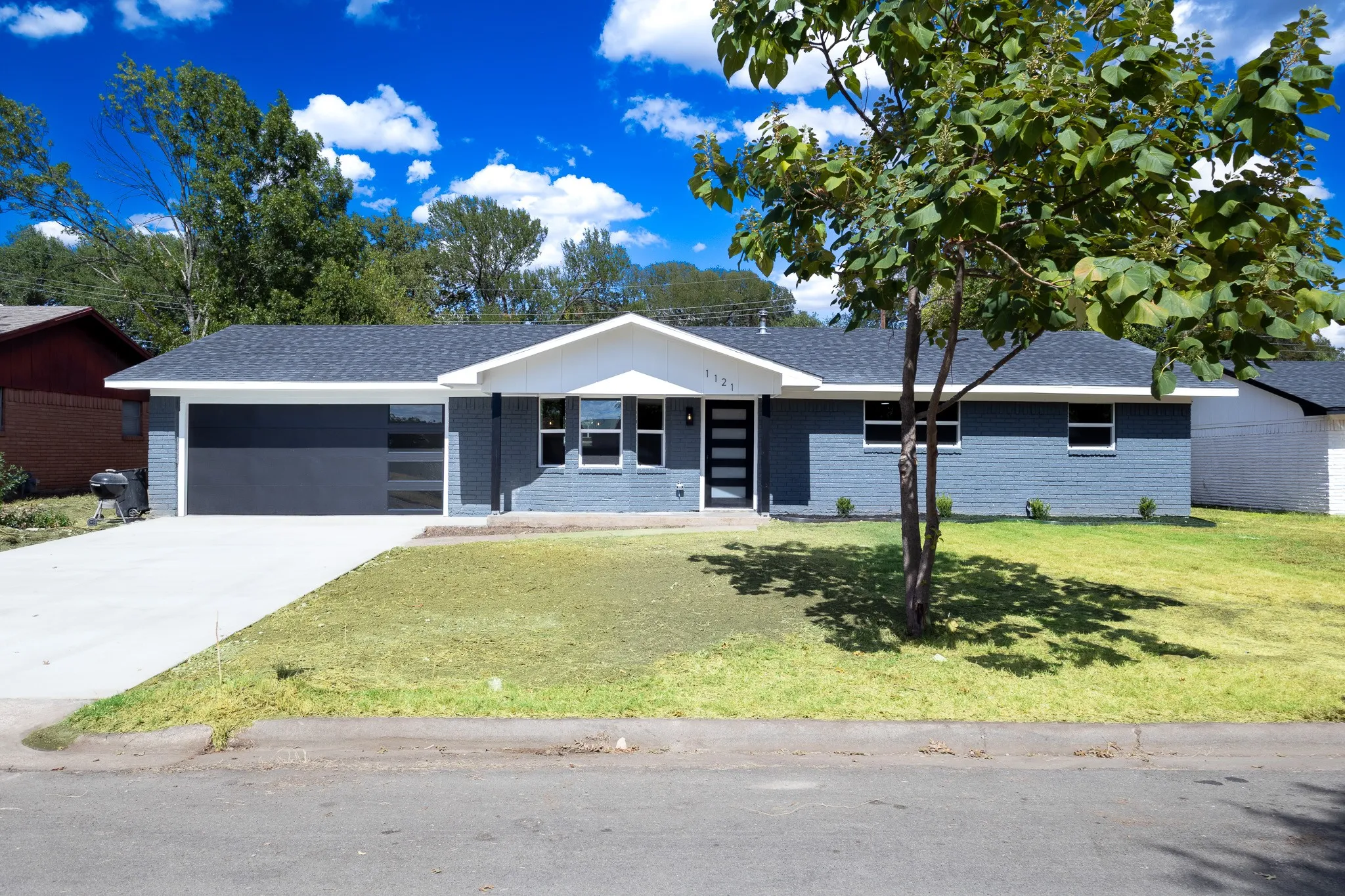 Single-story residence featuring a gray-painted brick exterior, a dark gray asphalt shingle roof, and a contemporary dark gray garage door with frosted glass panels