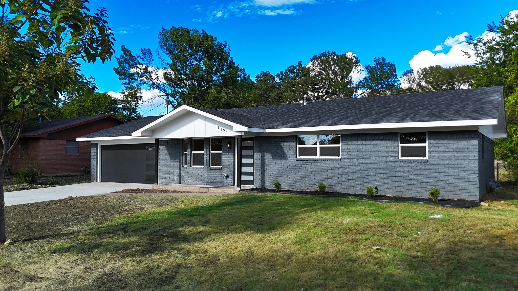 Single-story residence featuring a gray brick exterior, a dark shingle roof, a white gable accent, and a dark garage door