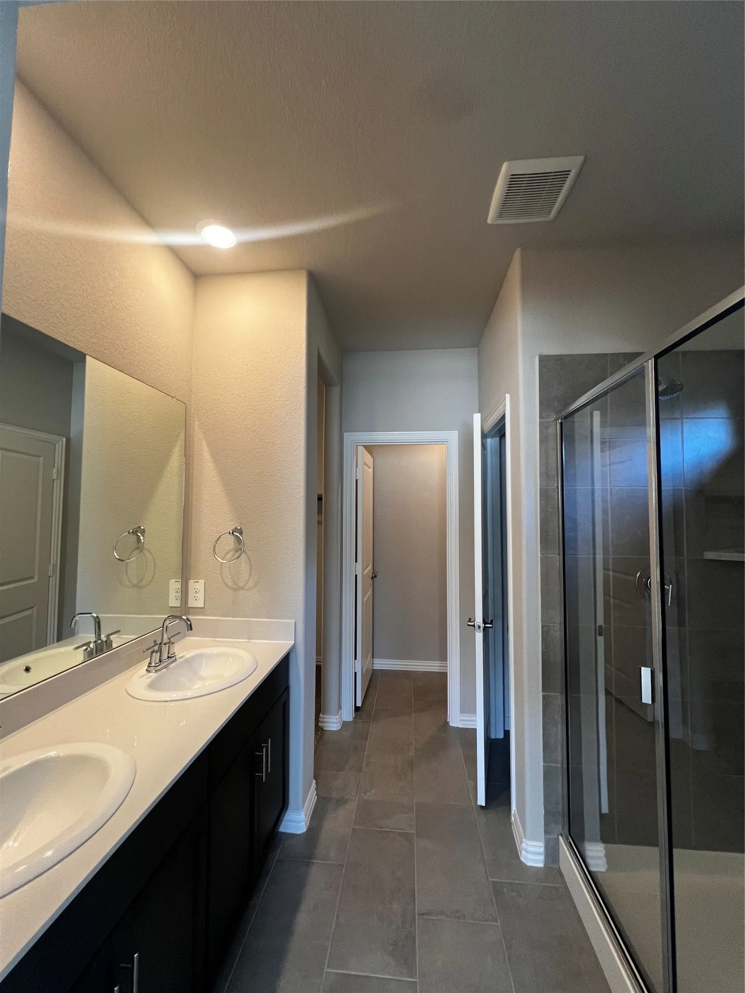 Dual vanity with integrated sinks, dark wood-finish cabinetry, frameless glass shower enclosure, and large format floor tiling