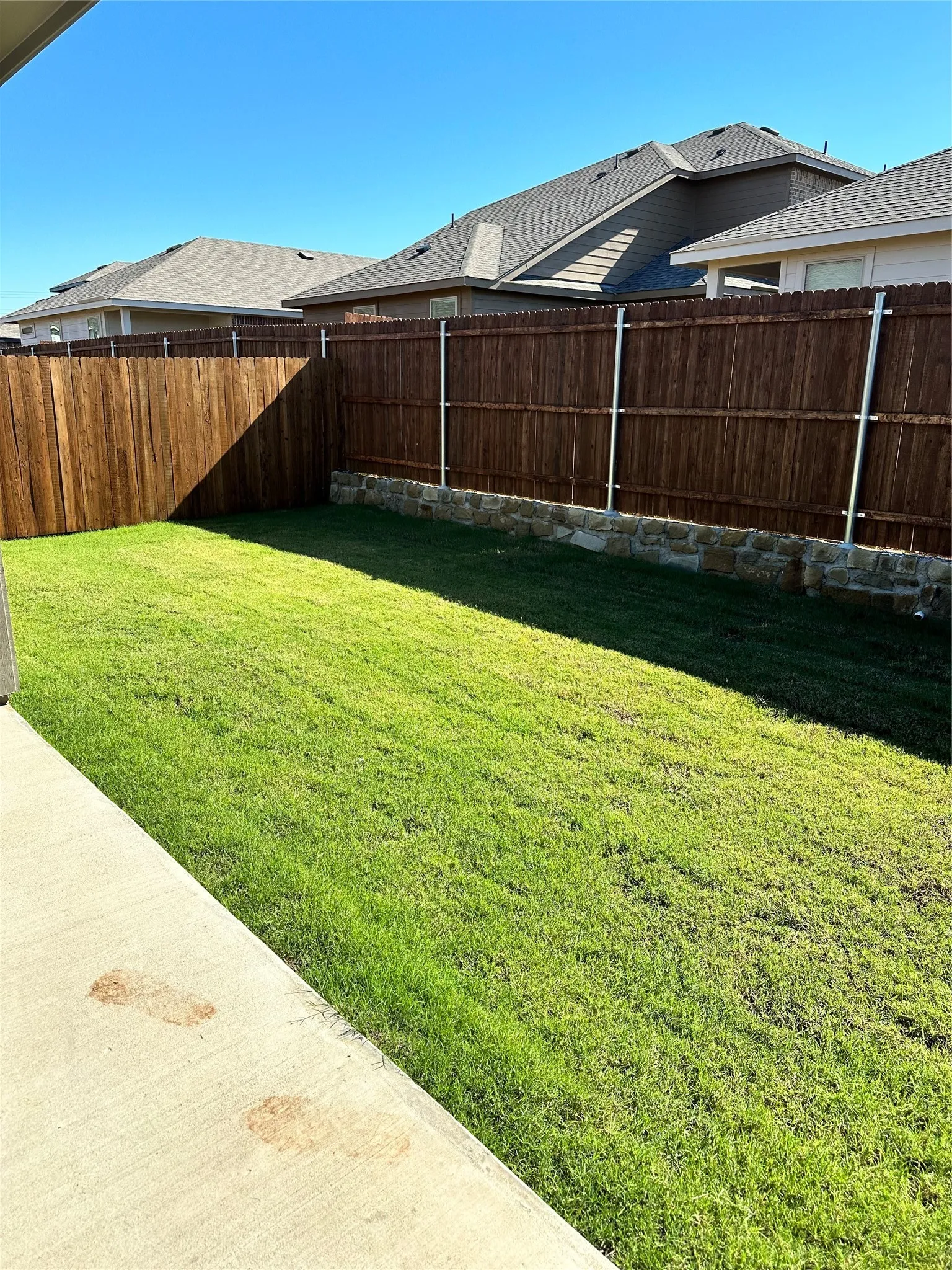 Expansive backyard featuring a manicured lawn, wood privacy fencing, and a stone retaining wall