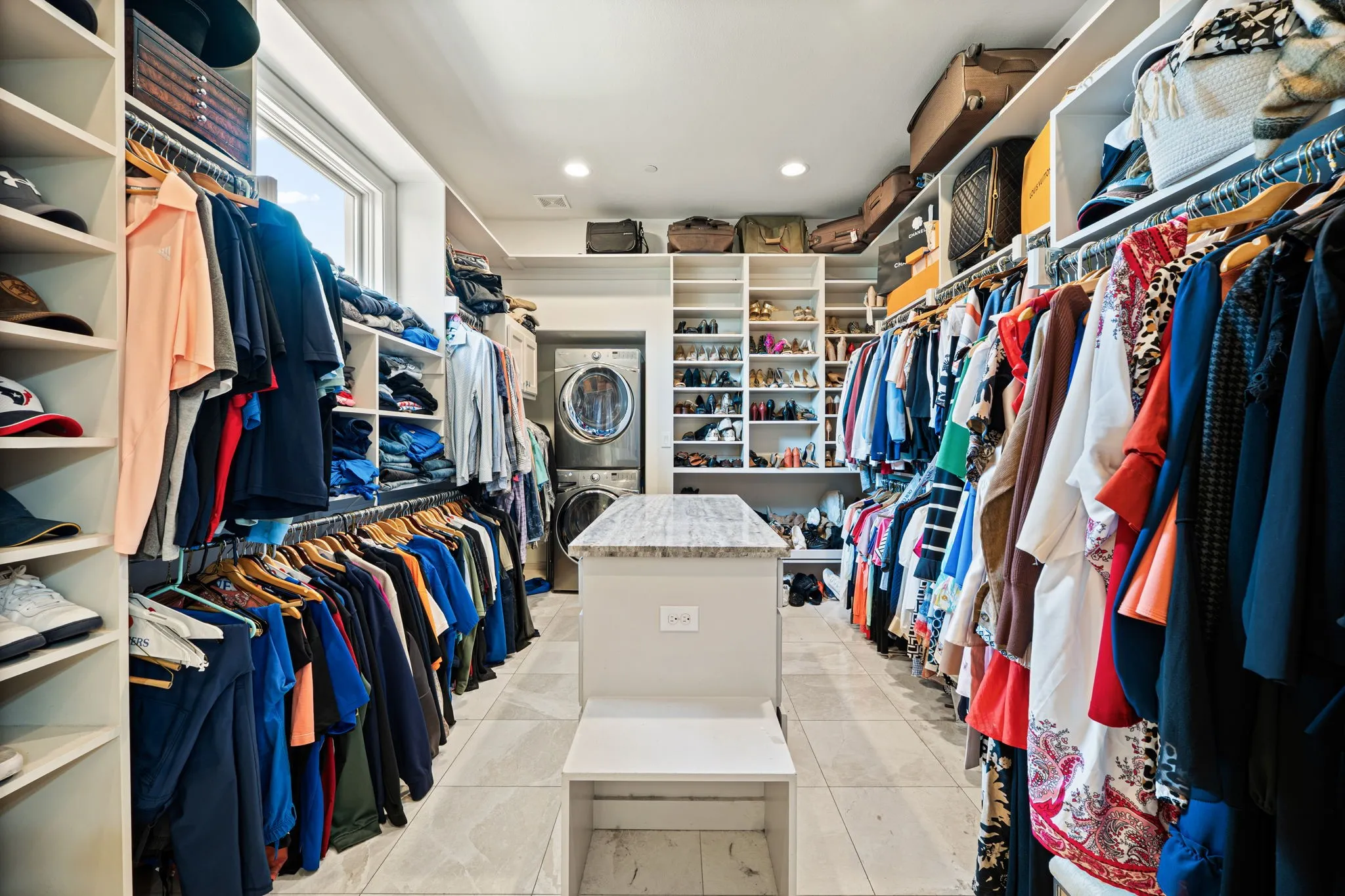 Expansive closet featuring built-in shelving, hanging rods, an integrated island with a stone countertop, and tile flooring