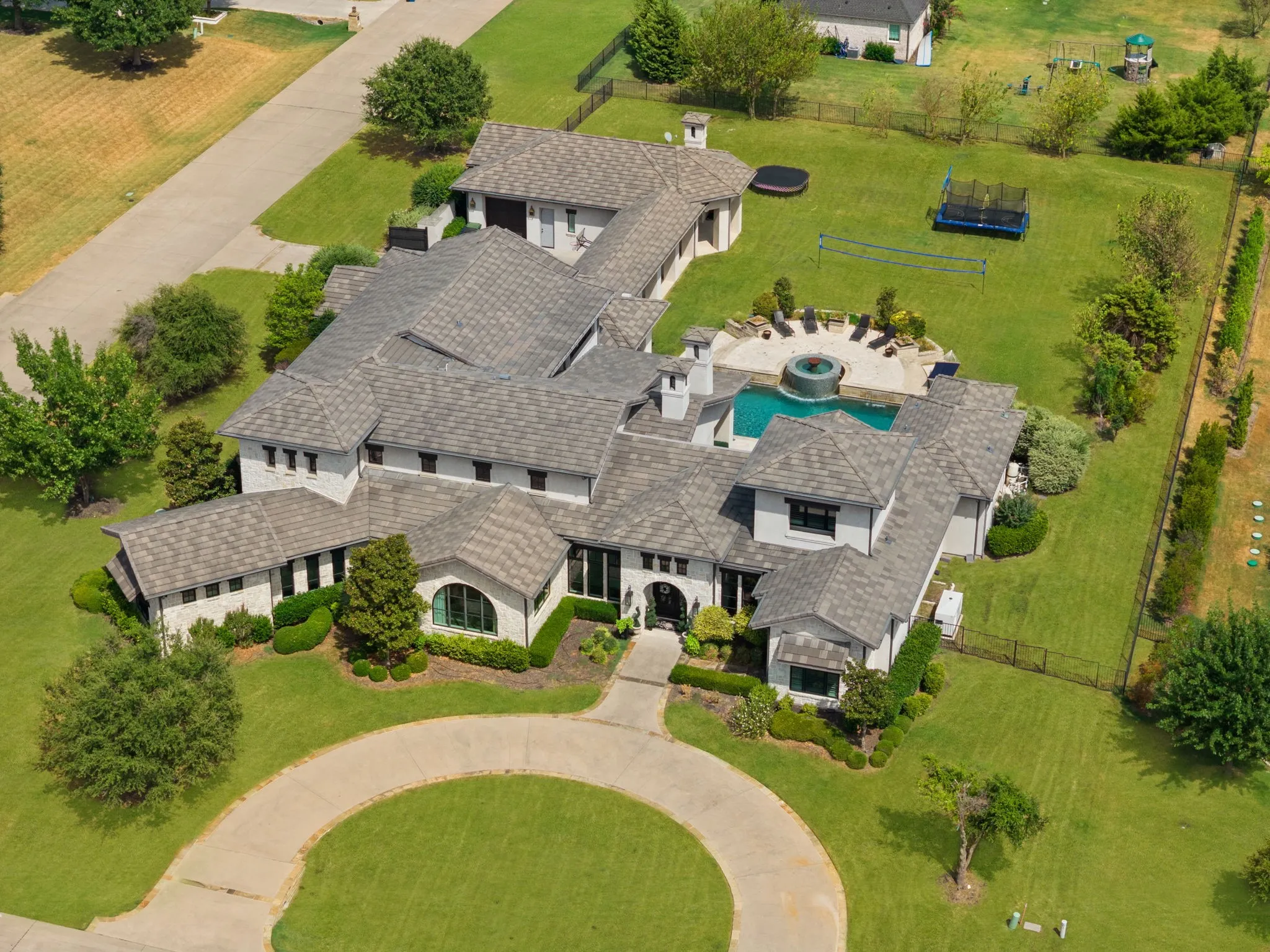 Expansive property featuring a circular driveway, multi-level tiled roofing, inground swimming pool with water feature, and extensive paved patio surround