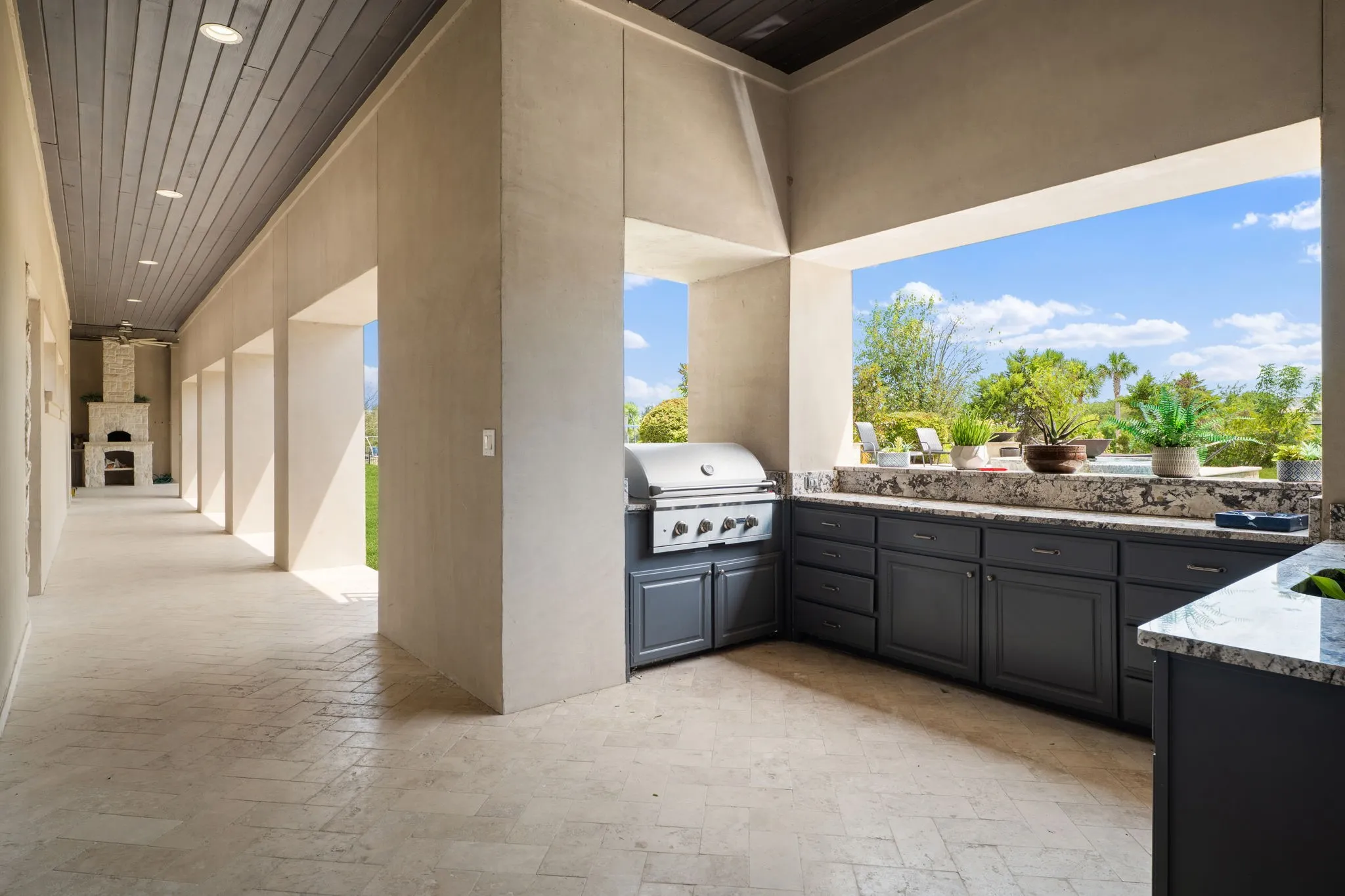 Outdoor covered patio featuring a built-in grill, extensive counter space, lower cabinetry, and a stone-finish fireplace