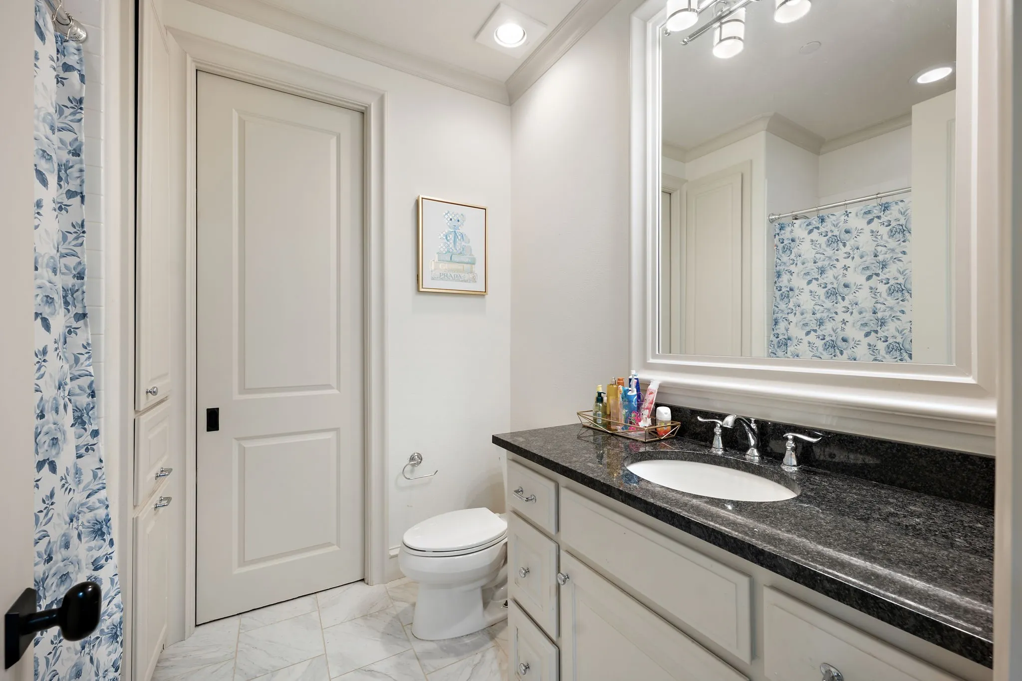 Vanity with dark countertop, undermount sink, white cabinetry, and polished chrome fixtures
