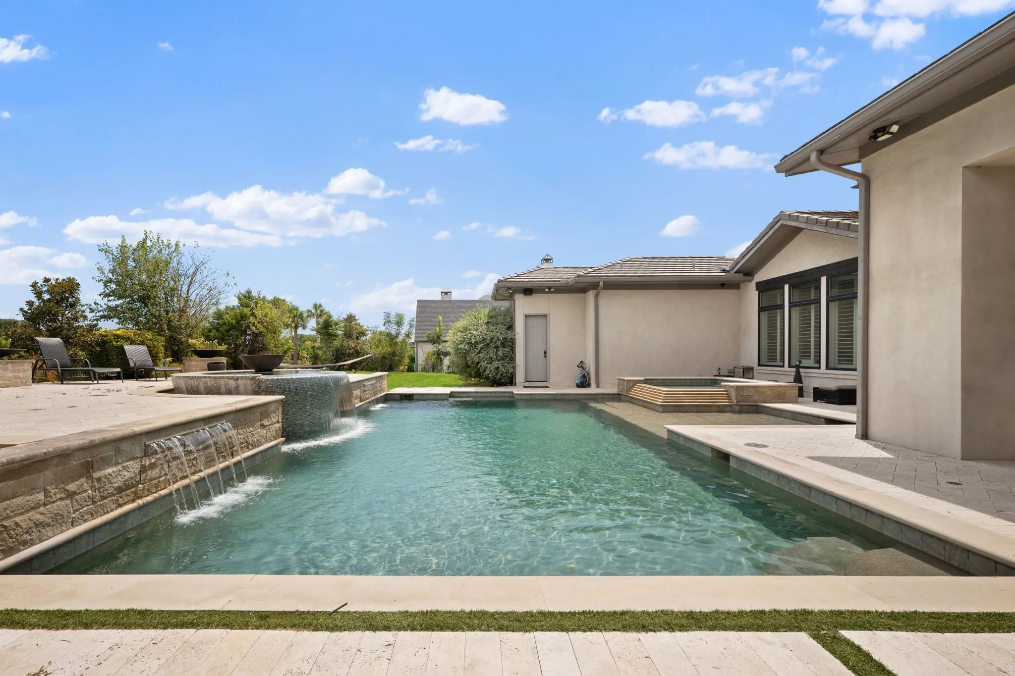 Outdoor swimming pool with integrated spa, waterfall features, and tiled water elements