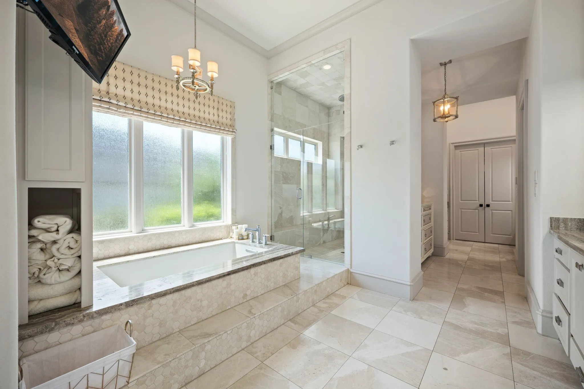 Built-in soaking tub with stone surround, glass-enclosed shower, dual pendant lighting, white cabinetry, and large format tile flooring
