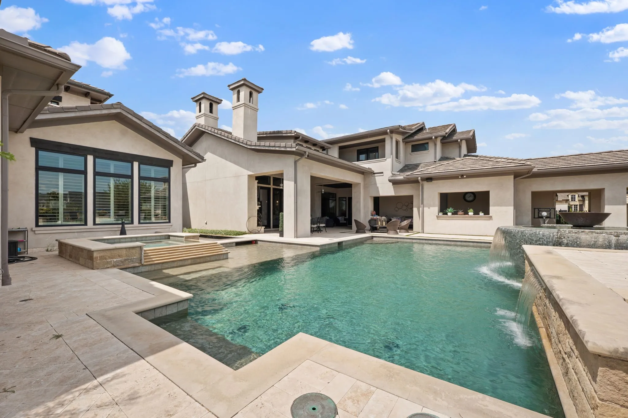 Exterior stucco finish, multiple chimneys, in-ground pool with integrated spa, waterfall feature, and covered outdoor living area