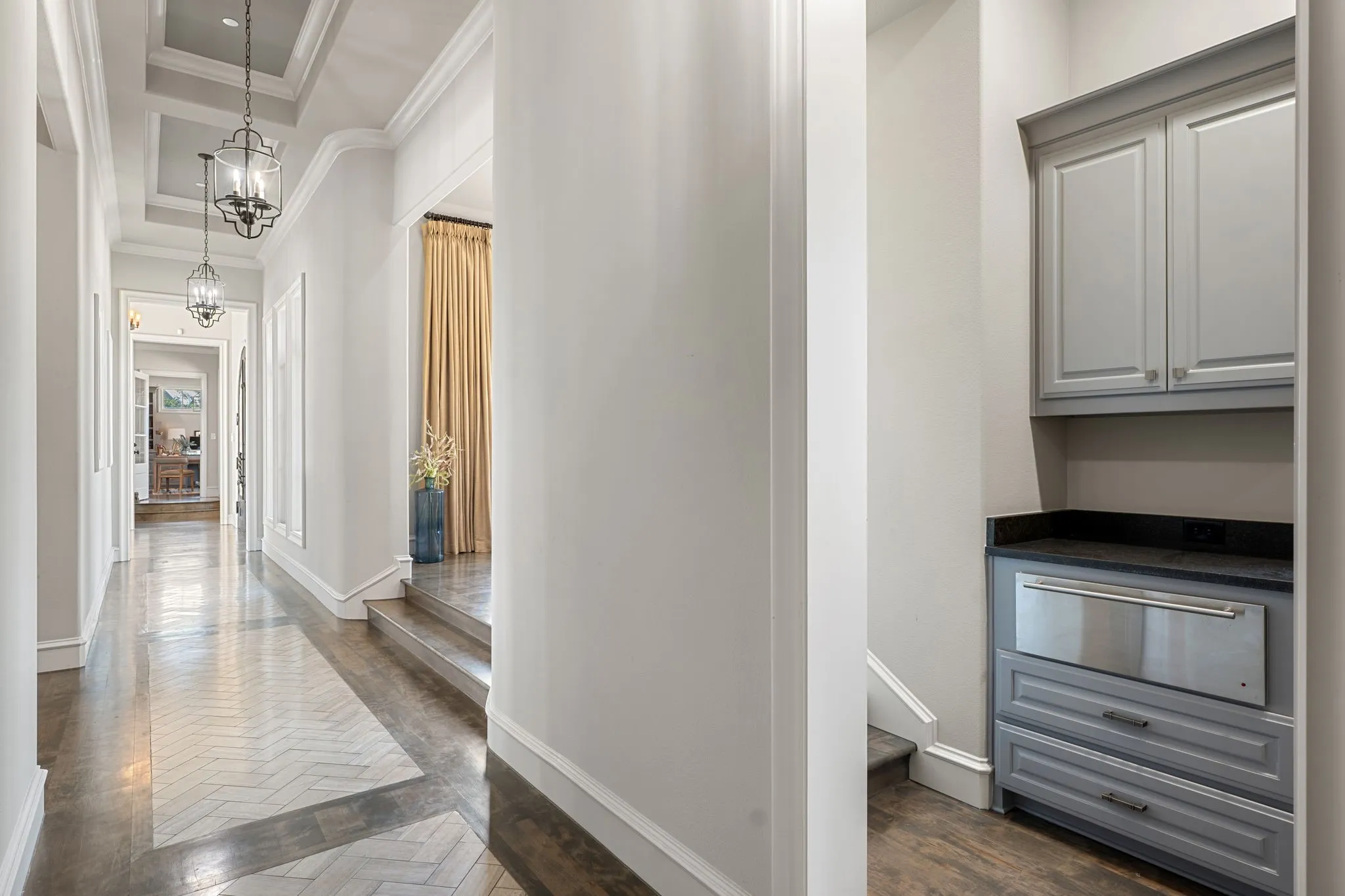 Hallway featuring coffered ceilings, decorative pendant lighting, and wood-finish flooring with a herringbone inlay