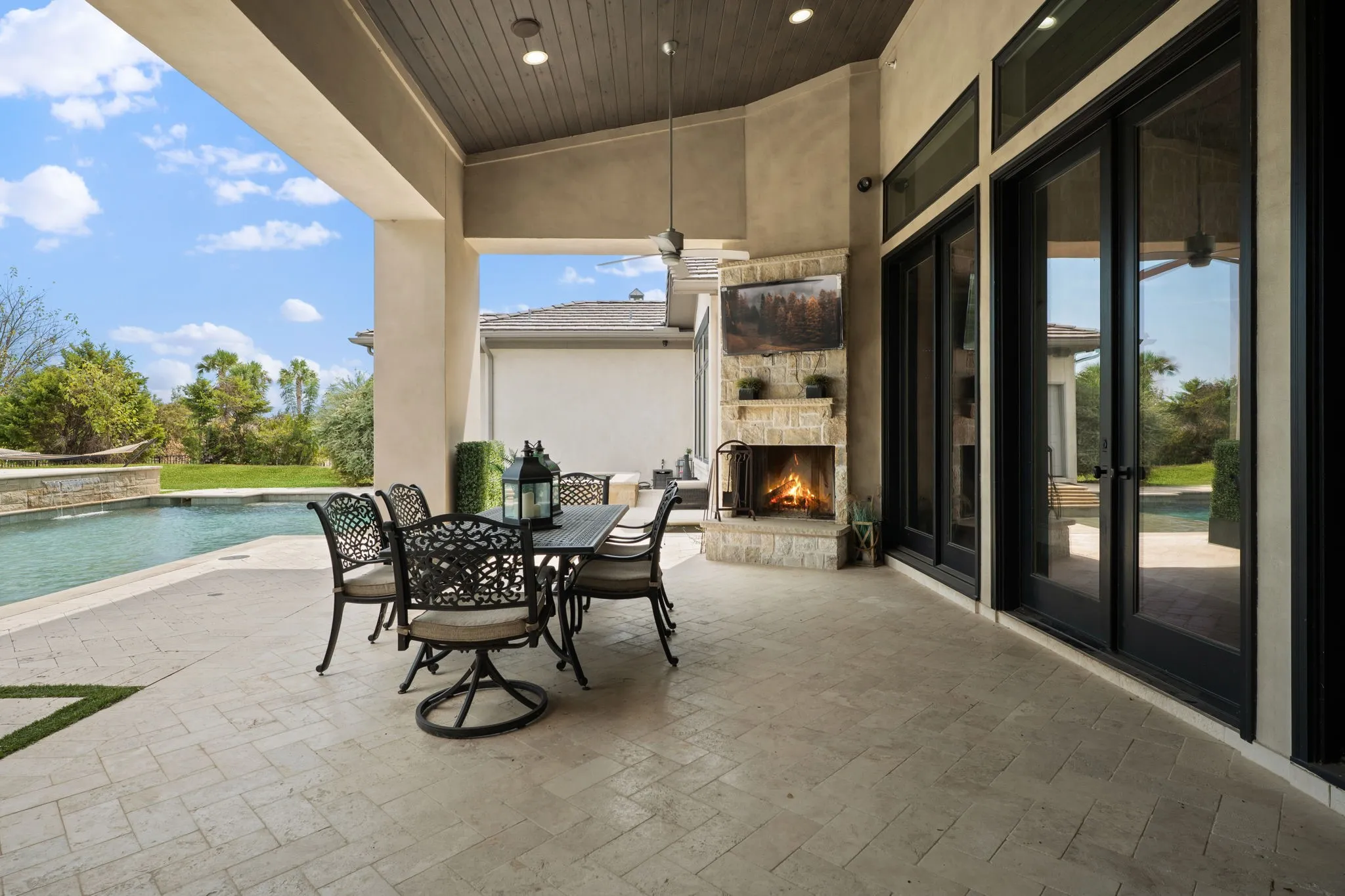 Covered patio featuring a stone fireplace, wood-plank ceiling, and black-framed glass doors