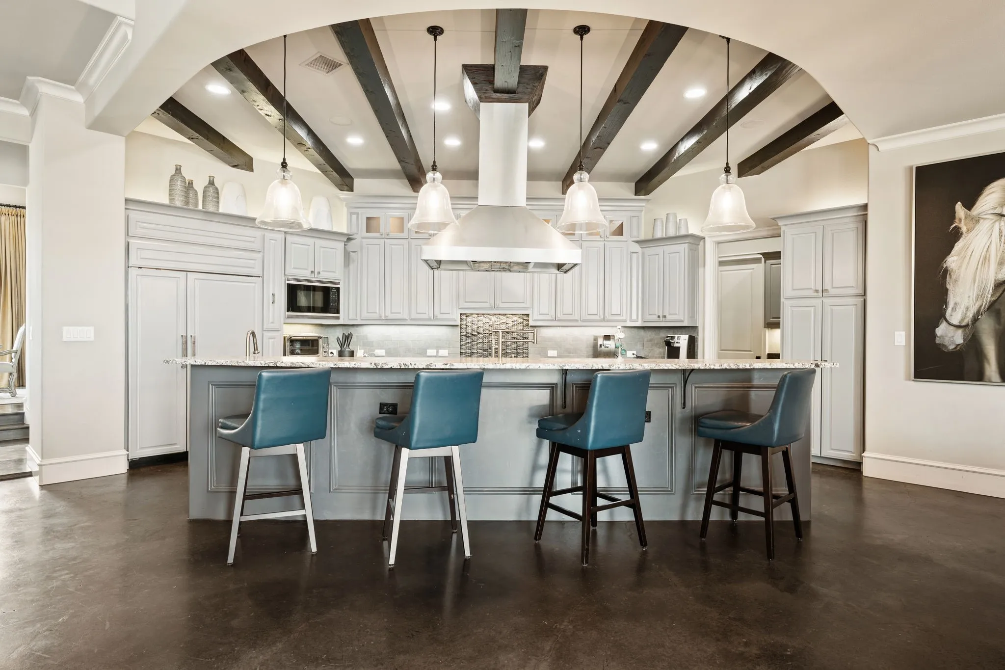 Kitchen featuring a large archway, recessed lighting, exposed ceiling beams, a central island with countertop seating, and light-toned cabinetry