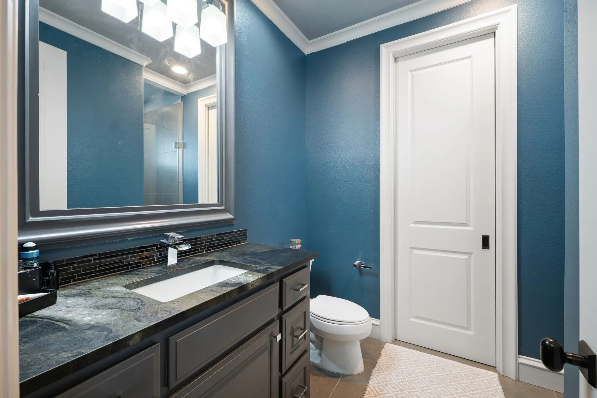 Vanity with a polished countertop, undermount sink, and dark subway tile backsplash