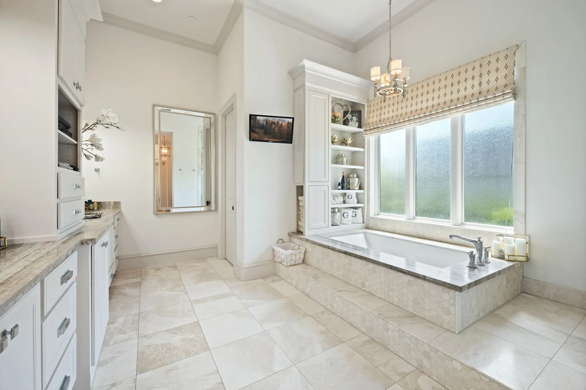 Soaking tub with a tiled surround, chandelier lighting, built-in shelving, vaulted ceiling, and dual vanity with stone countertops