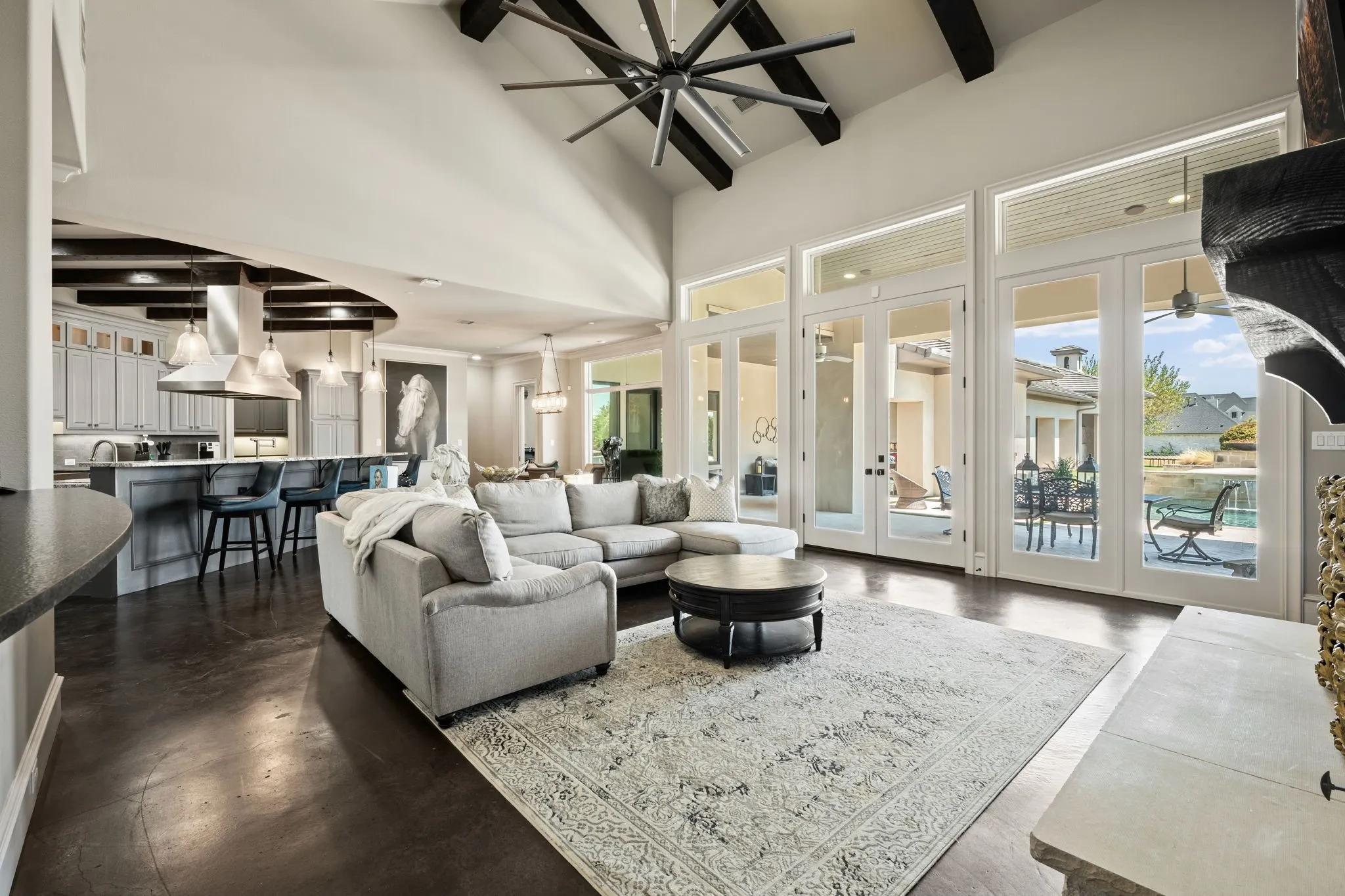 Vaulted ceiling with exposed wood beams, expansive glass doors, dark wood-finish flooring, and a built-in kitchen island with pendant lighting