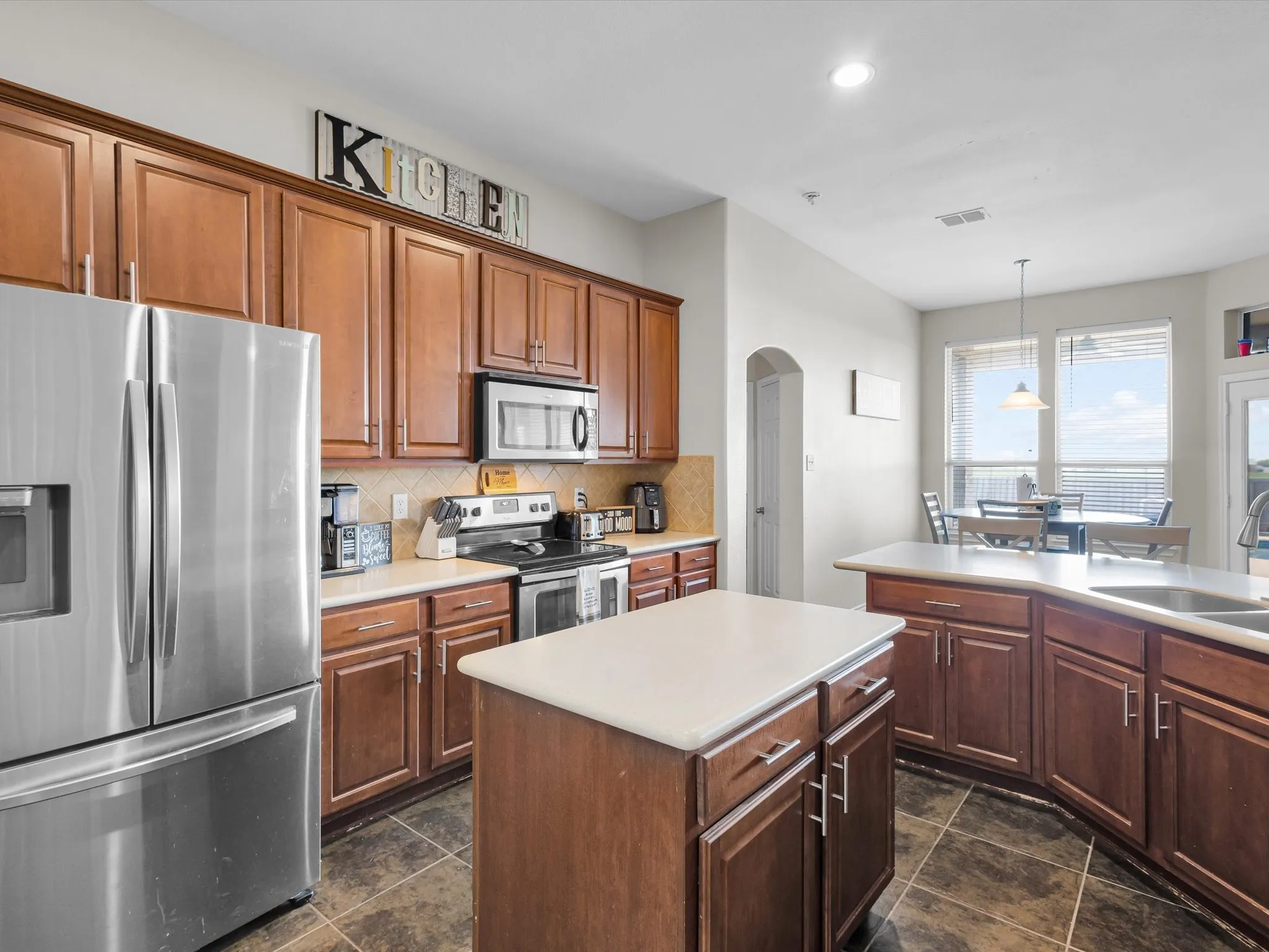 Kitchen featuring a stainless steel French door refrigerator, wood cabinetry, tile flooring, and an island with a light-colored countertop