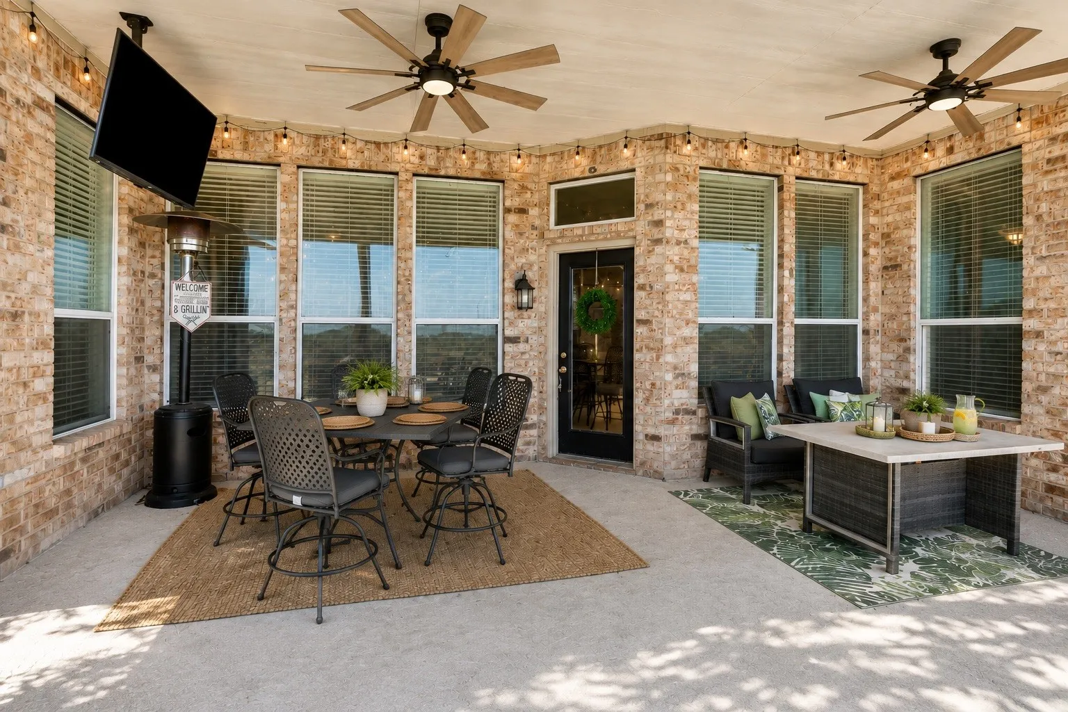 Covered patio with brick exterior, multiple ceiling fans, recessed string lighting, and a dark-framed glass paneled door