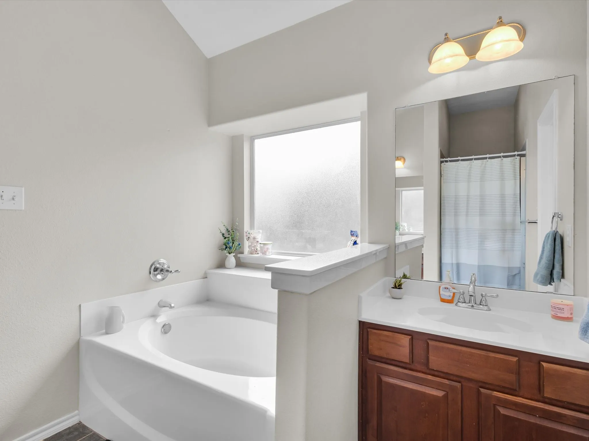Built-in soaking tub with chrome fixtures, frosted glass window, single vanity with wood-finish cabinetry, and overhead lighting