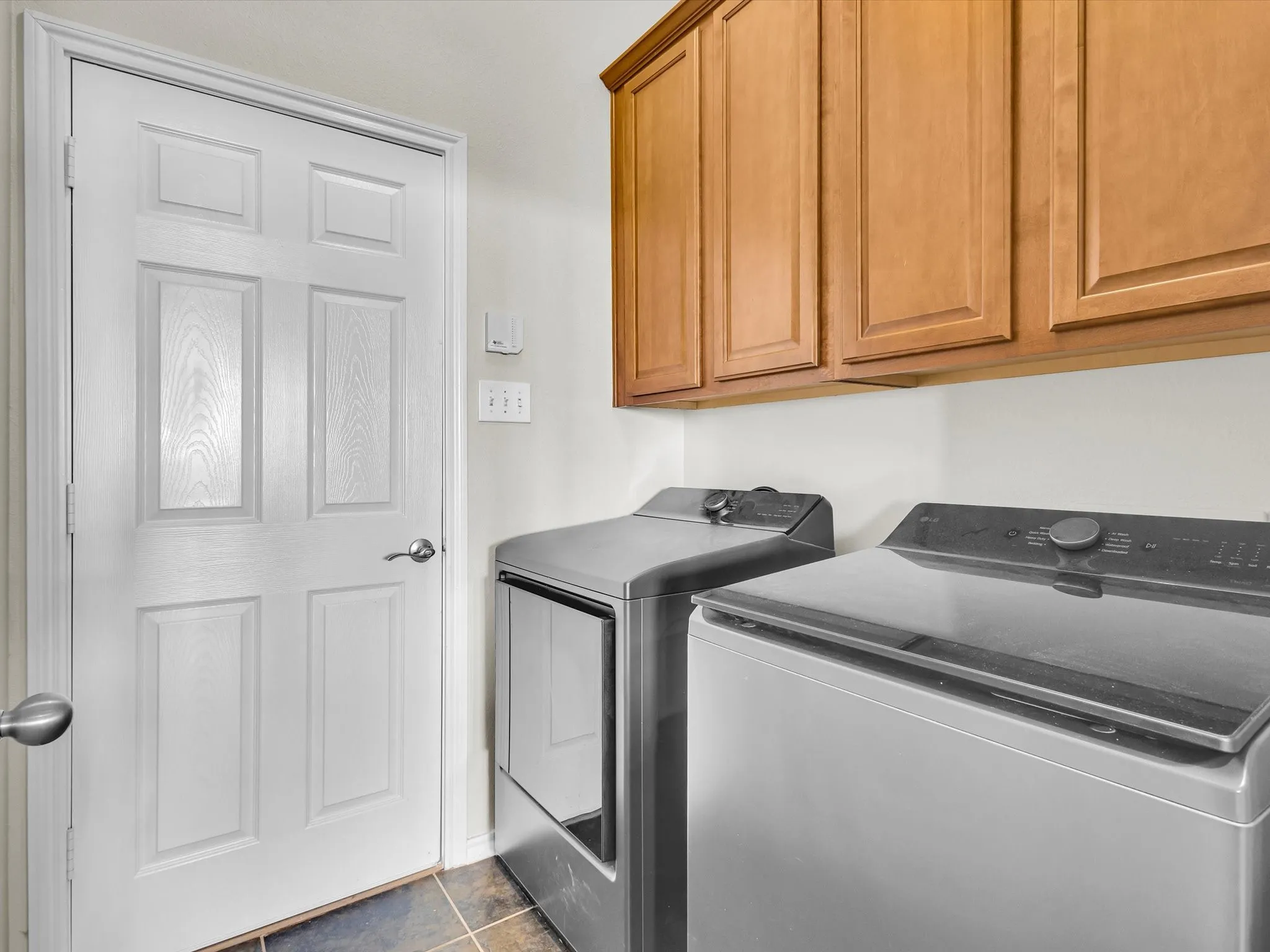 Wood-finish upper cabinetry, paneled white door, and tiled flooring