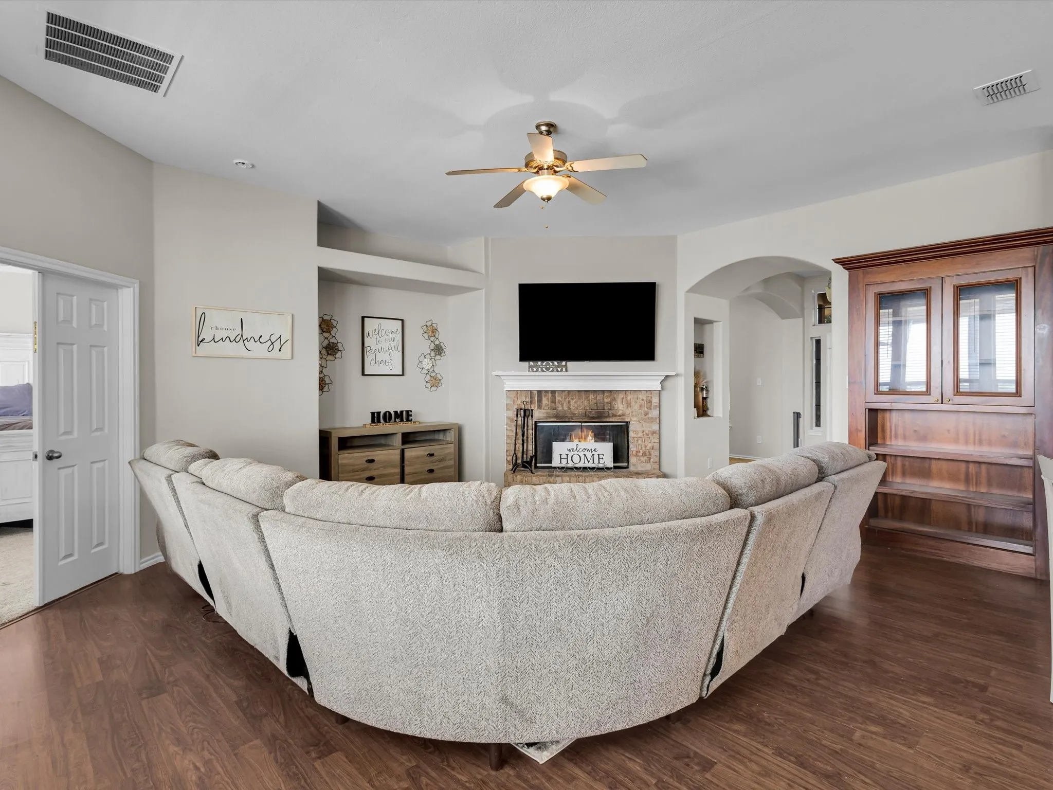 Wood-finish flooring throughout, ceiling fan with integrated lighting, built-in fireplace with stone surround, arched doorway, and a built-in wood-finish display cabinet