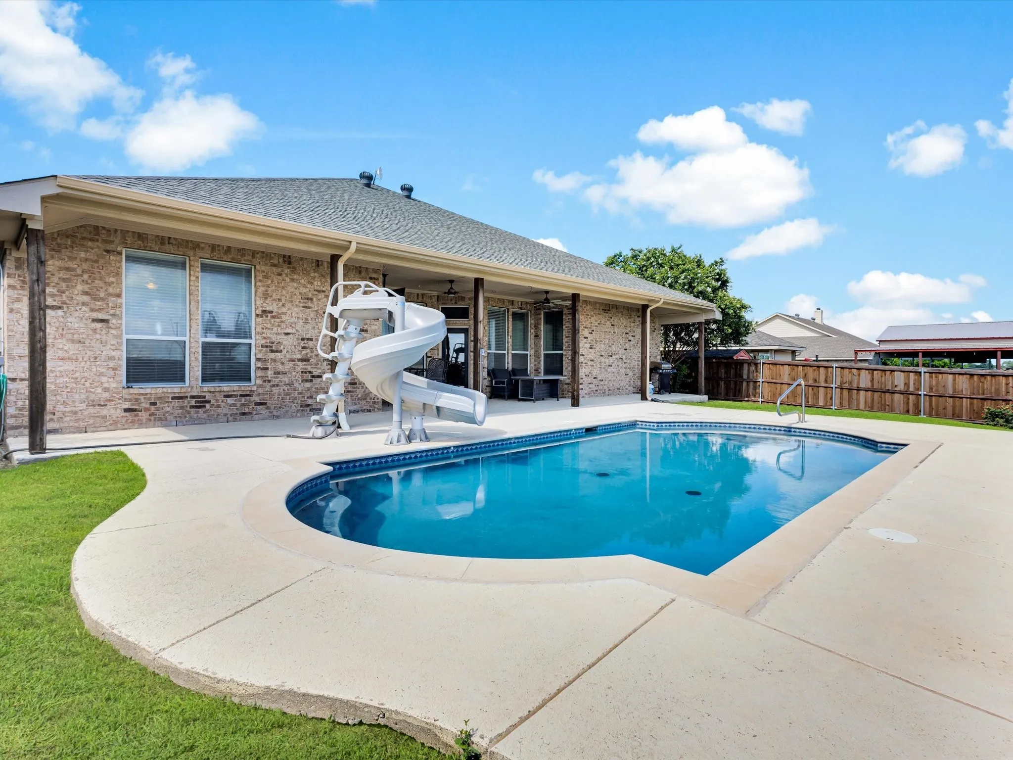 Brick exterior with an in-ground swimming pool, concrete surround, and a covered patio area
