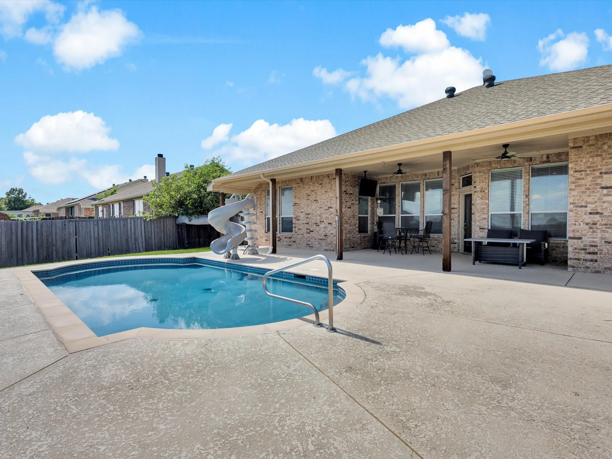 Expansive backyard with a built-in swimming pool and slide, generous concrete patio, and a covered porch featuring exposed wood-finish posts and ceiling fans