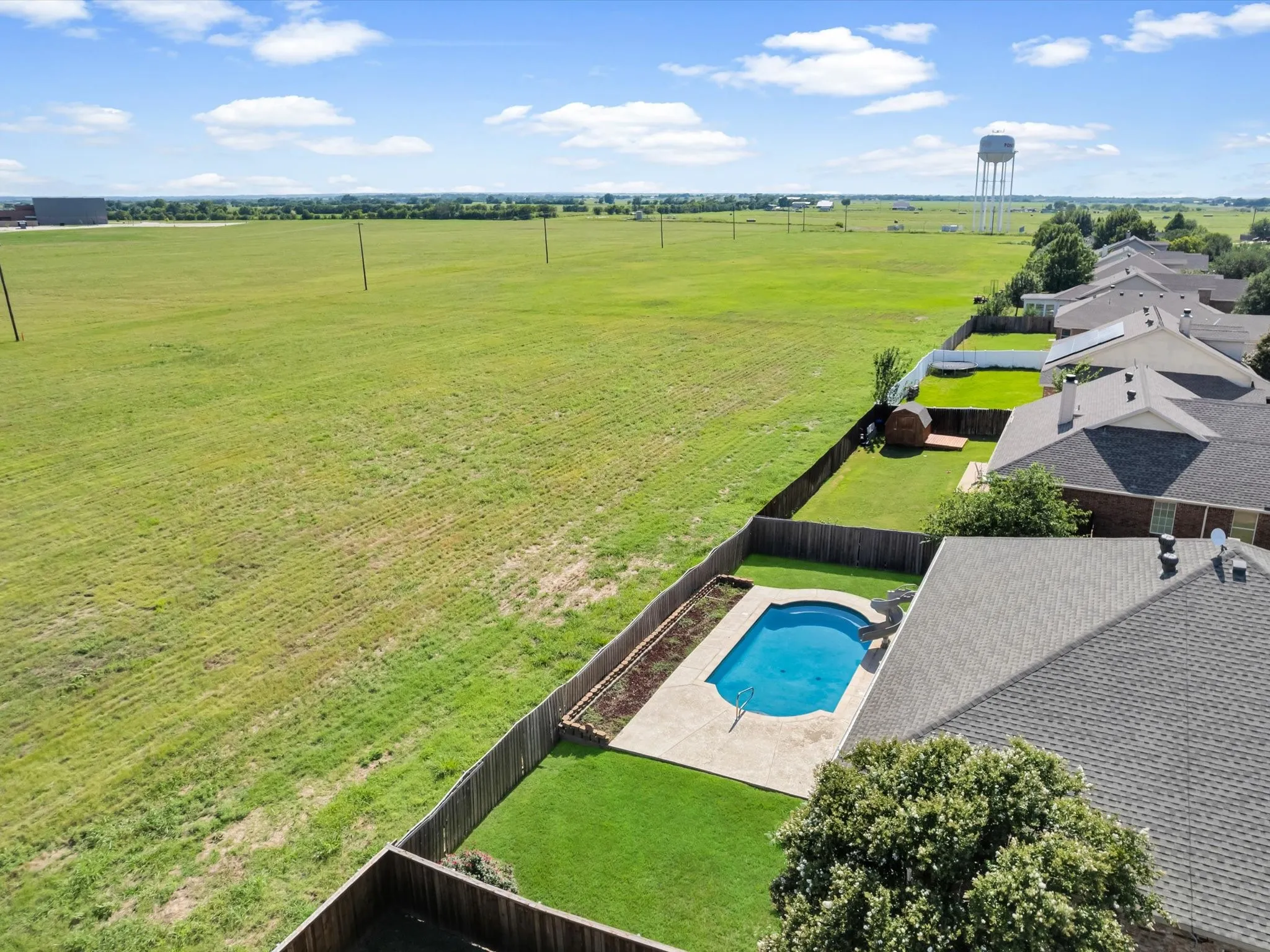 Backyard featuring a clear blue swimming pool, concrete pool decking, manicured lawn, and a wooden privacy fence