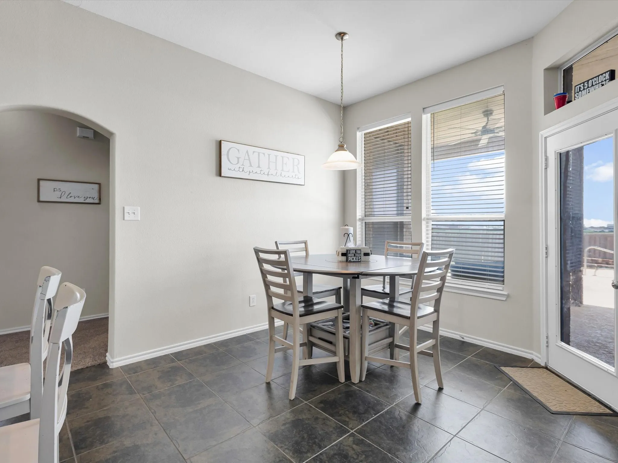 Tiled flooring, multiple windows with blinds, a glass-paneled door, and an arched doorway