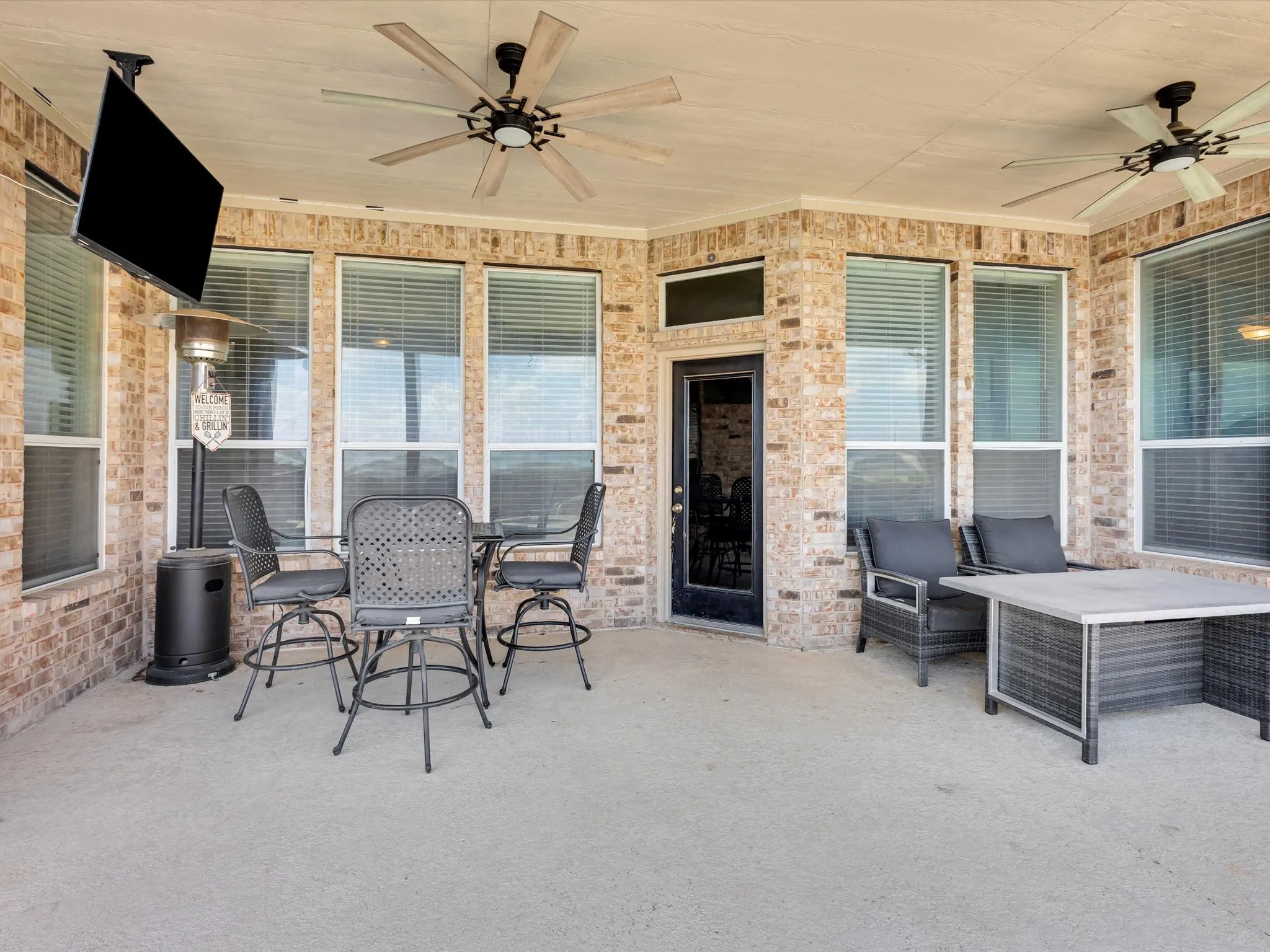 Covered patio featuring brick exterior walls and multiple windows with blinds