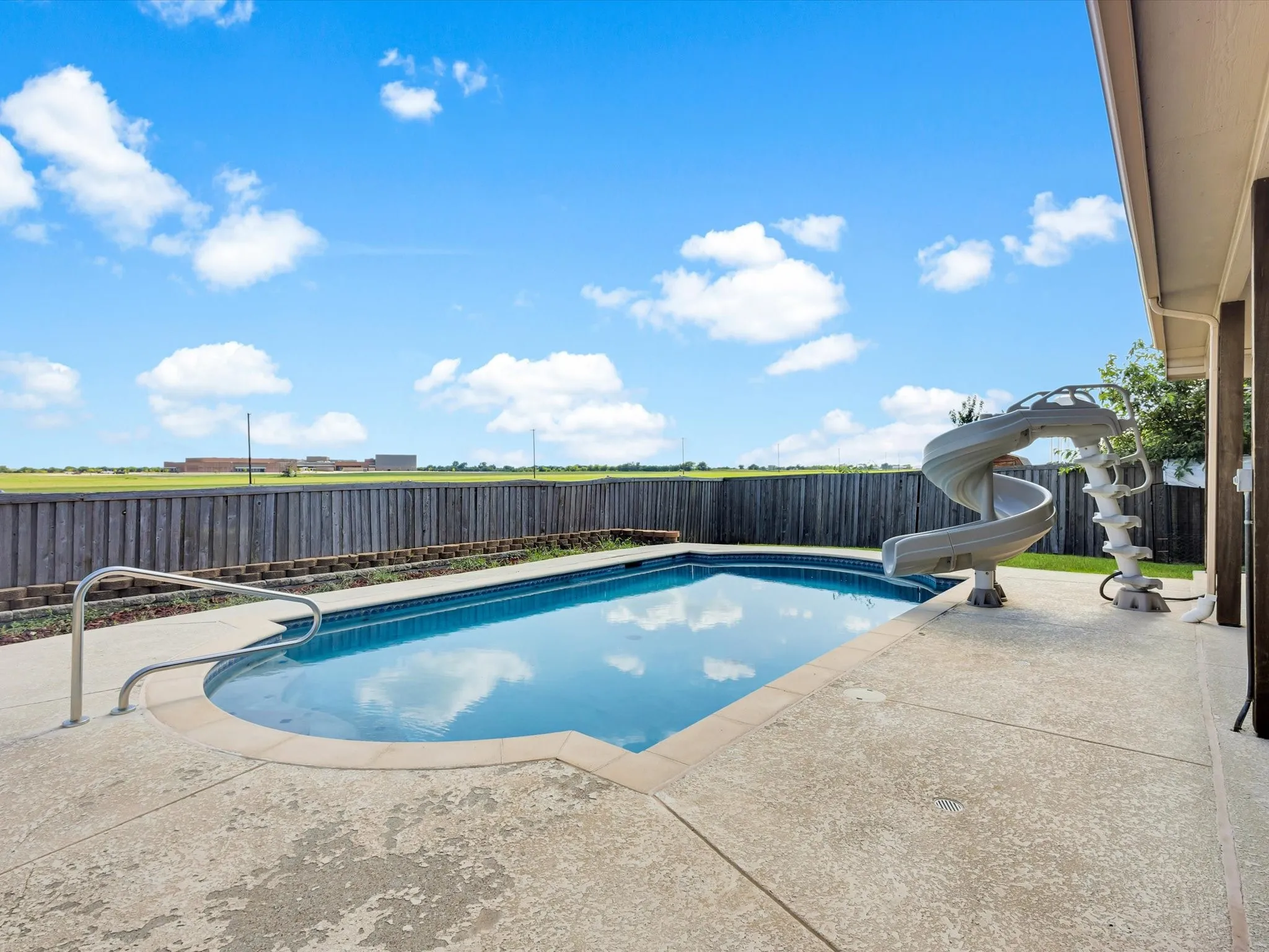 Outdoor swimming pool with integrated slide, surrounded by a concrete patio and a perimeter privacy fence