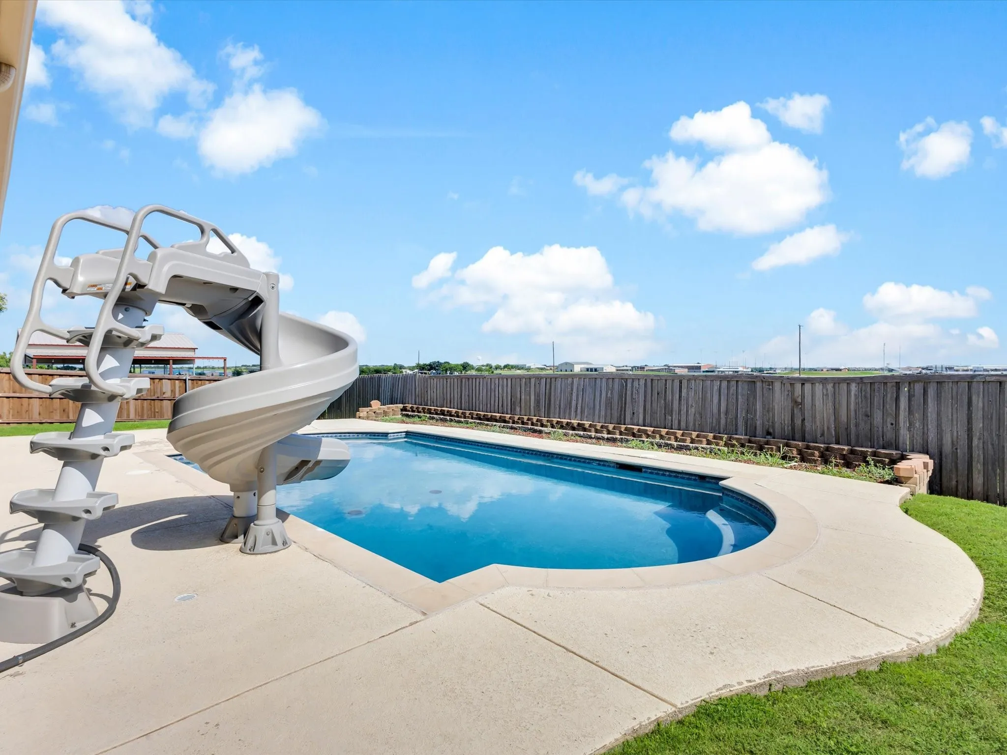 Curved inground pool with concrete decking, a spiral waterslide, and a wood privacy fence