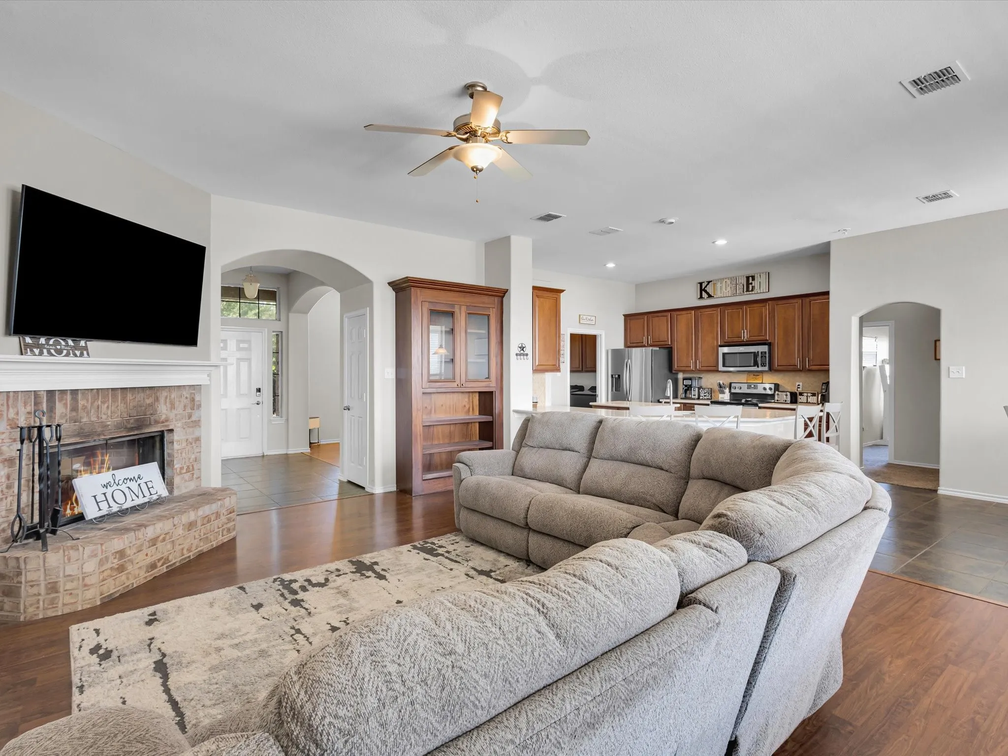 Brick fireplace with mantel, ceiling fan with light fixture, arched doorways, wood-finish flooring, and recessed lighting